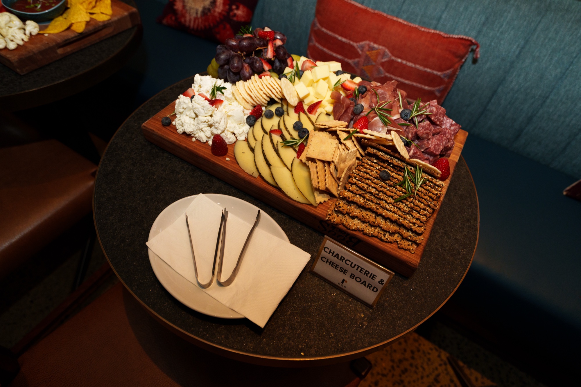 Wooden charcuterie and cheese board with grapes, crackers and berries on a round black table