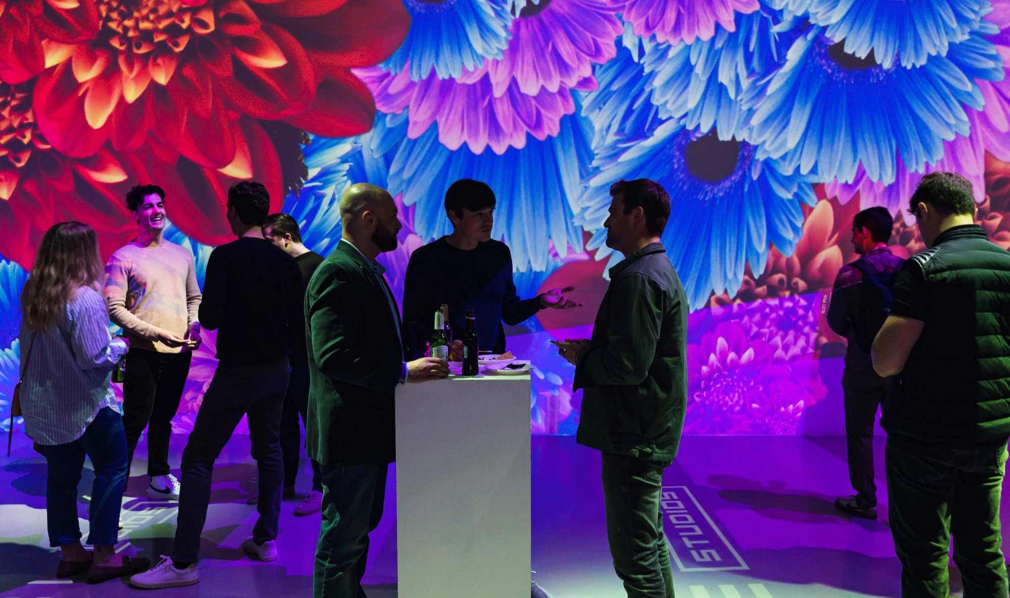 Guests talk in front of giant projected red and blue flowers at the Metaplex event
