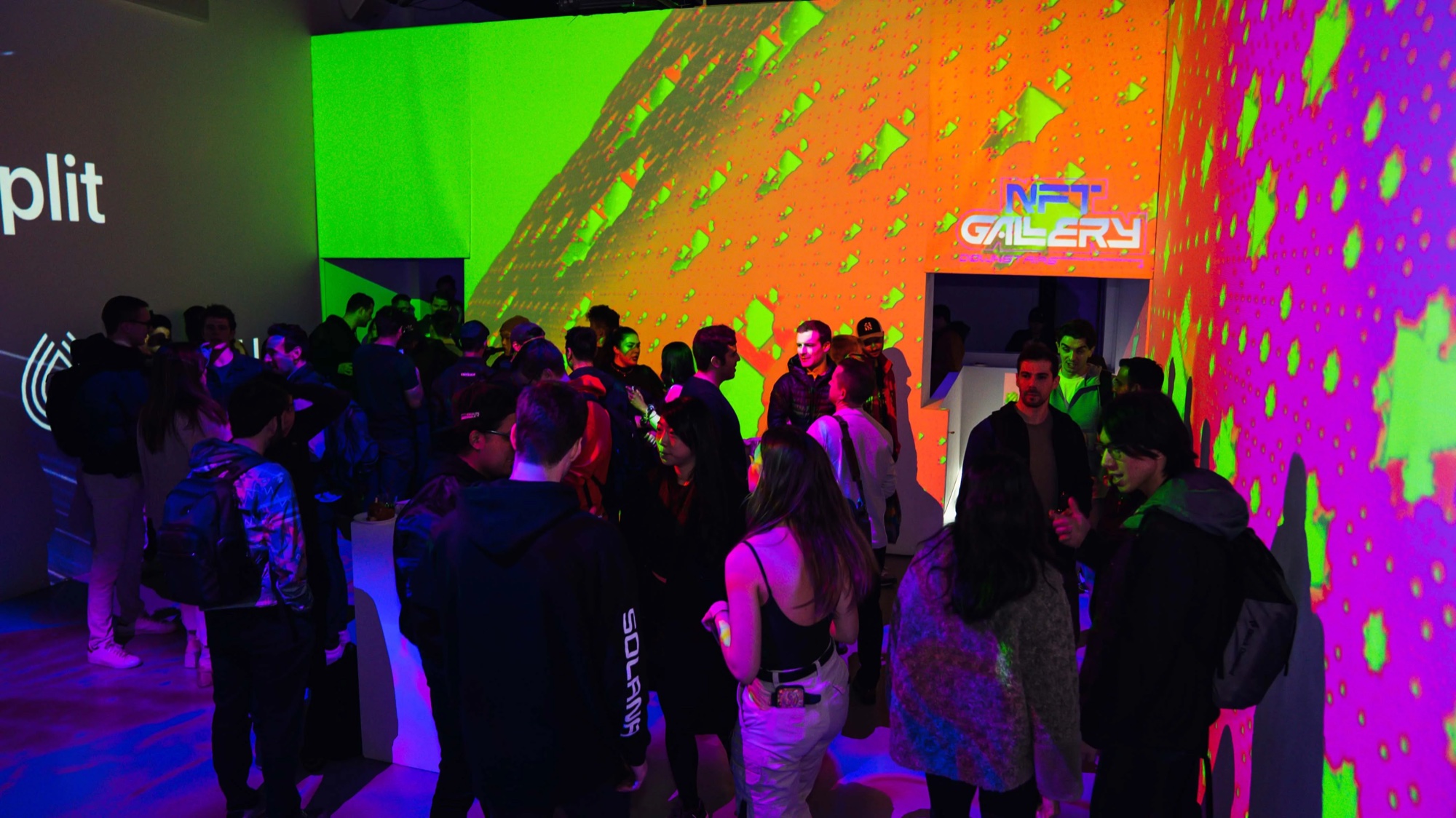 Guests under green and orange geometric projections beside an NFT Gallery sign
