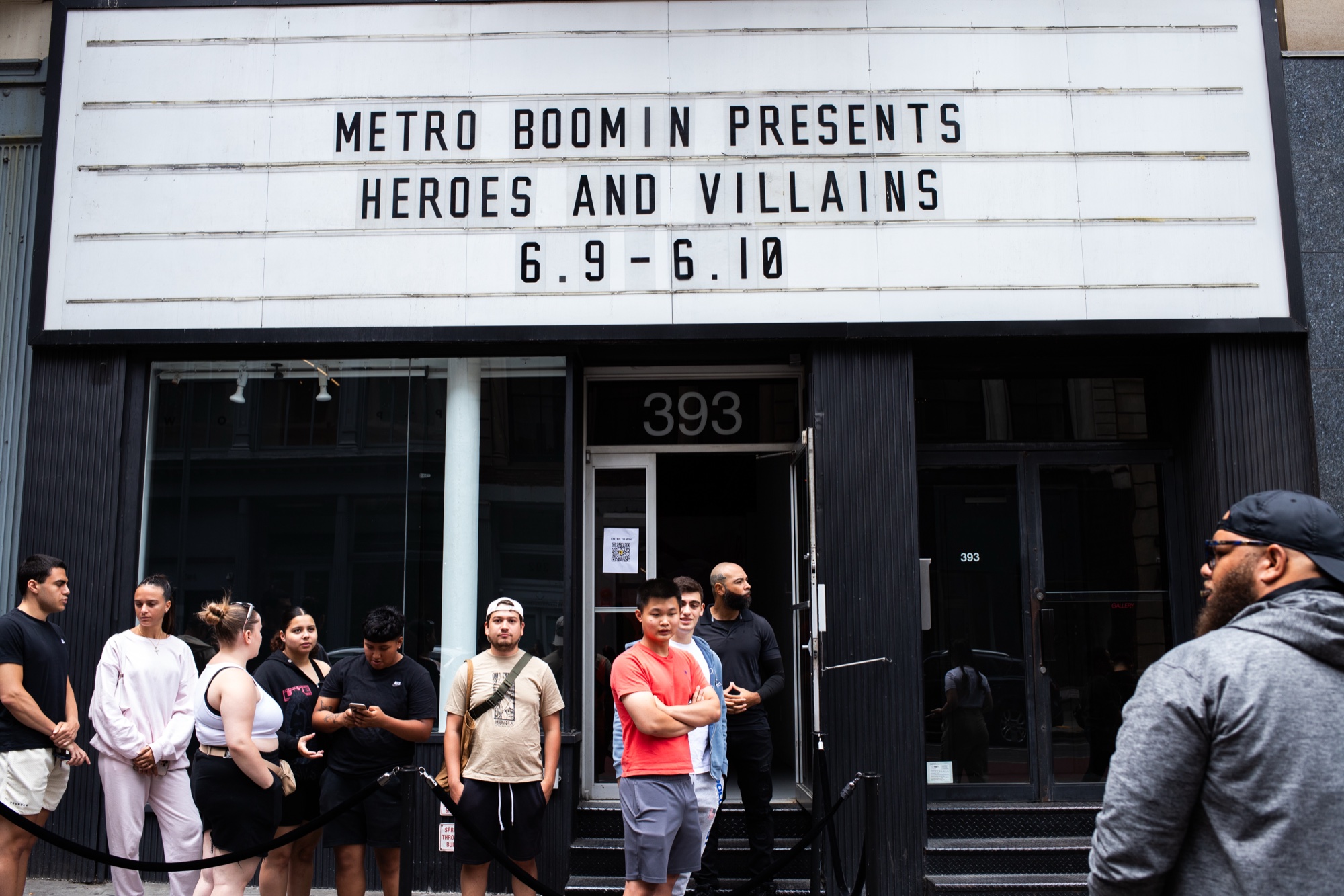 People queue outside a marquee reading Metro Boomin Presents Heroes and Villains on a city street