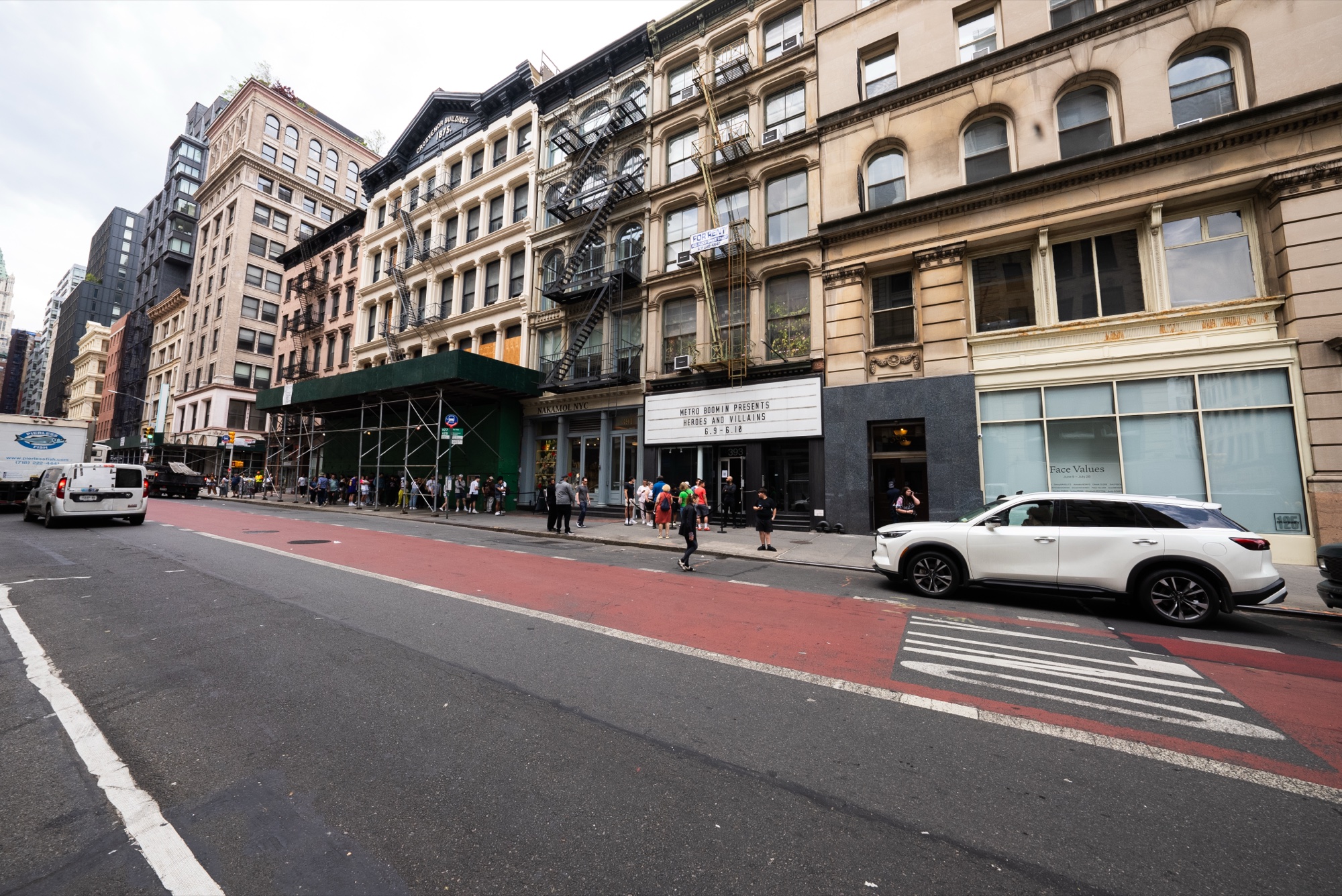 A white SUV waits on a red bus lane outside a marquee on a block of cast iron Manhattan buildings
