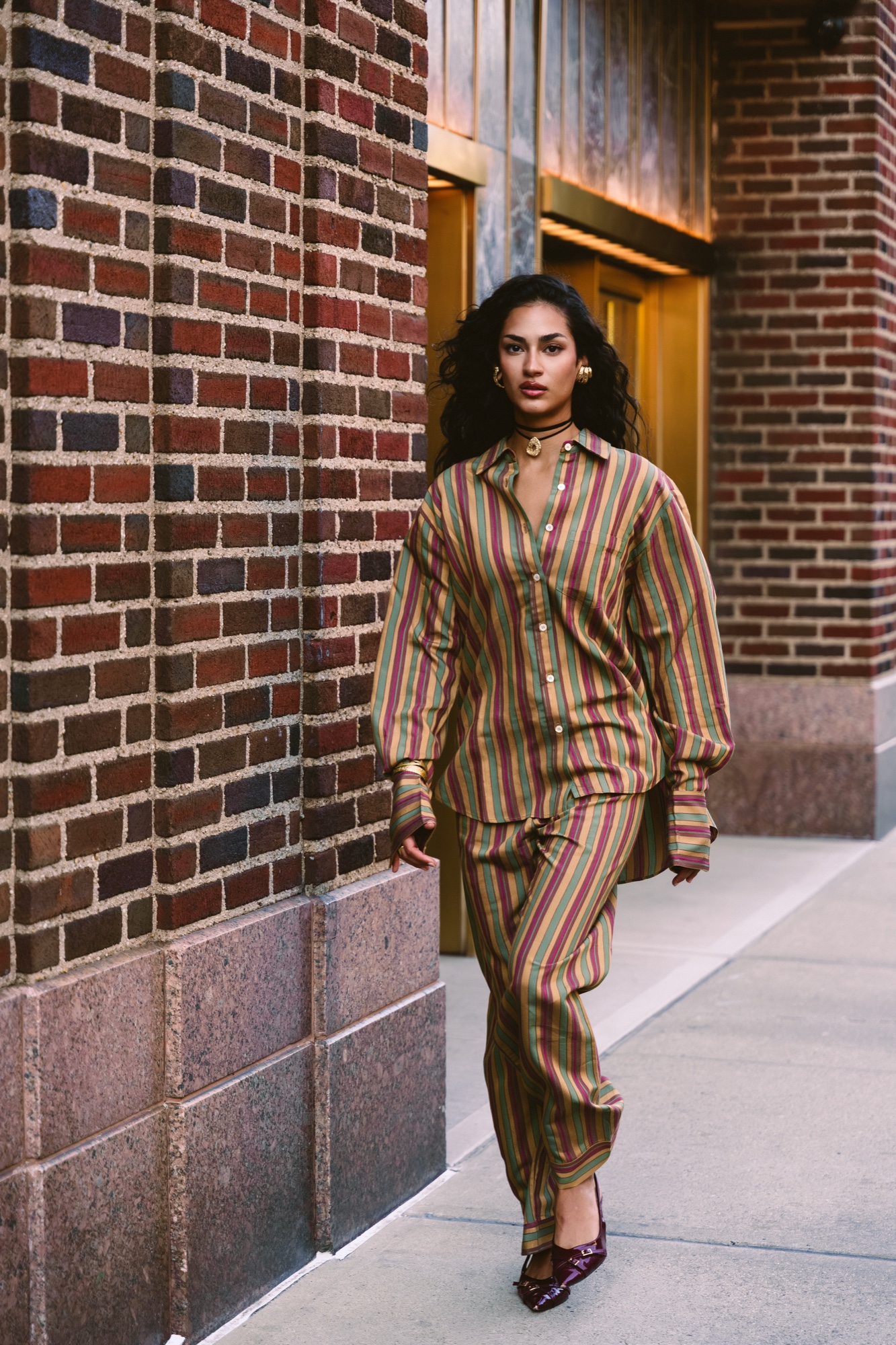 Woman in a striped shirt and trousers walking past brick walls and brass doors in Manhattan