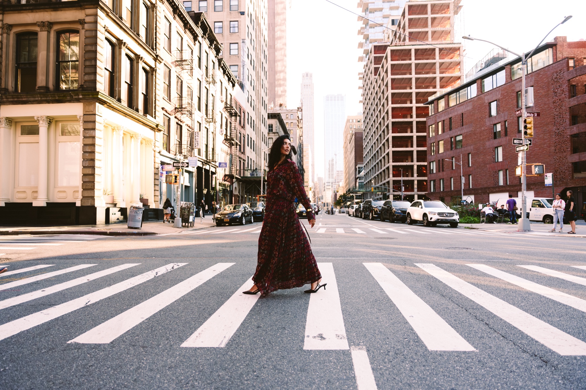 A woman in a long red patterned dress crosses a wide Manhattan crosswalk with tall buildings behind