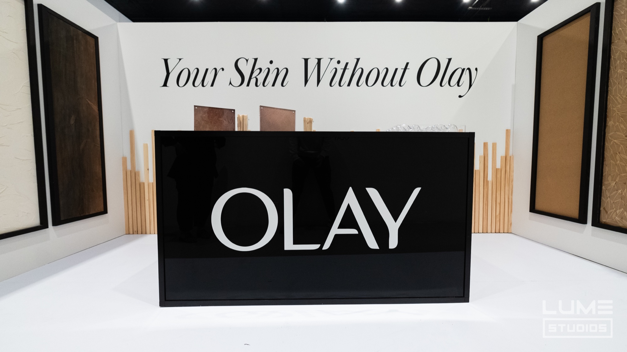 Black Olay box lit on a white set with the words Your Skin Without Olay on the wall behind