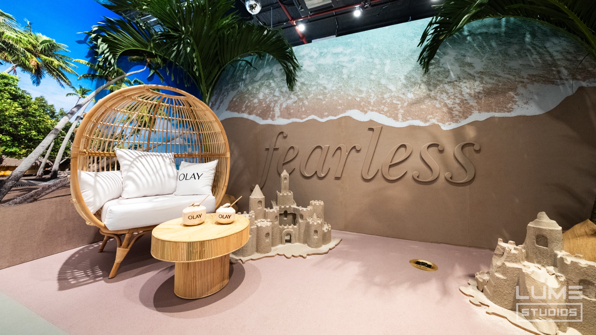 A rattan egg chair and round tables sit before a sand wall reading fearless beside sandcastles and a beach backdrop