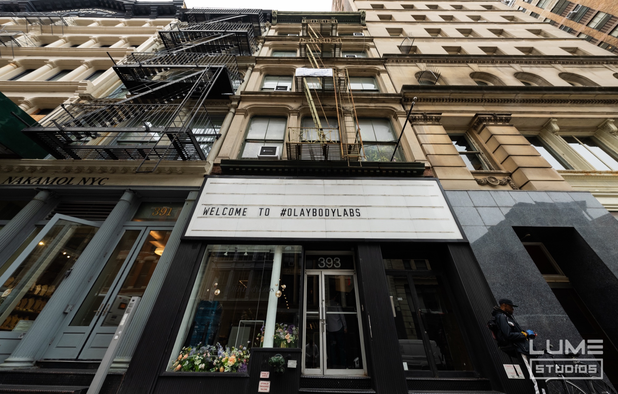 Narrow cast iron storefront with a marquee reading Welcome To #OlayBodyLabs among taller Manhattan buildings