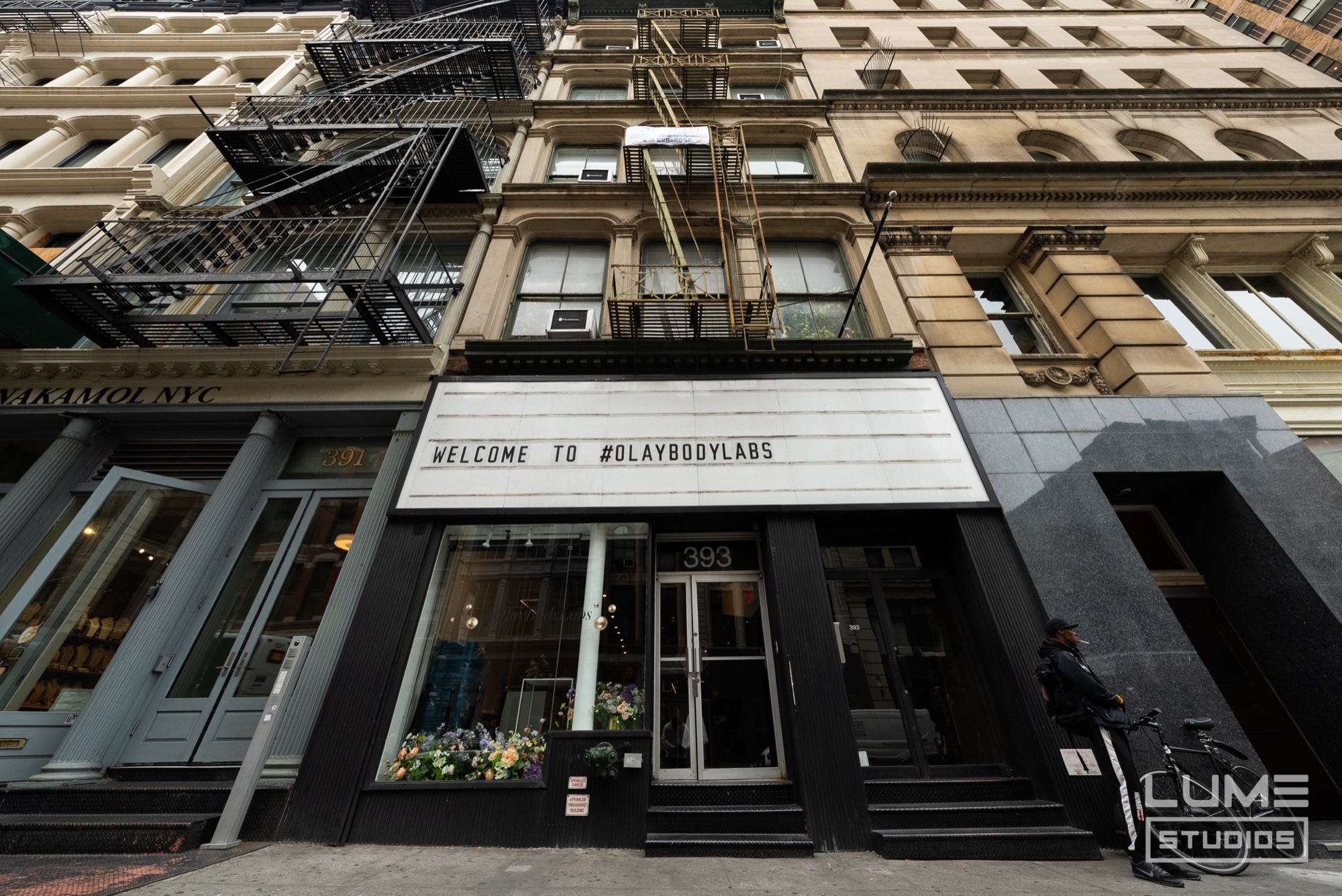 Cast iron building with fire escapes above a black storefront marquee reading welcome to #olaybodylabs