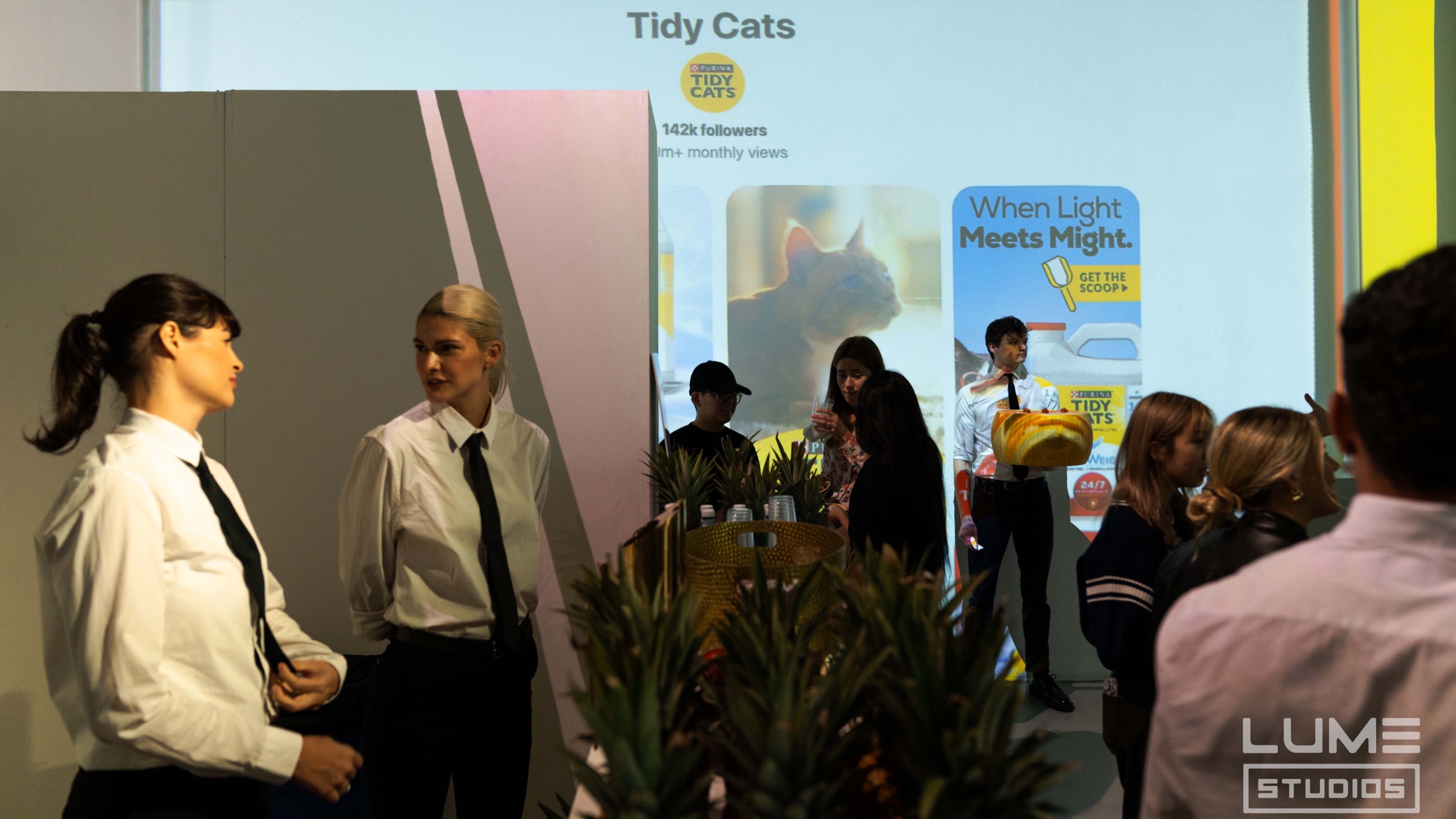Servers in ties stand before a Tidy Cats slide during the Pinterest marketing event