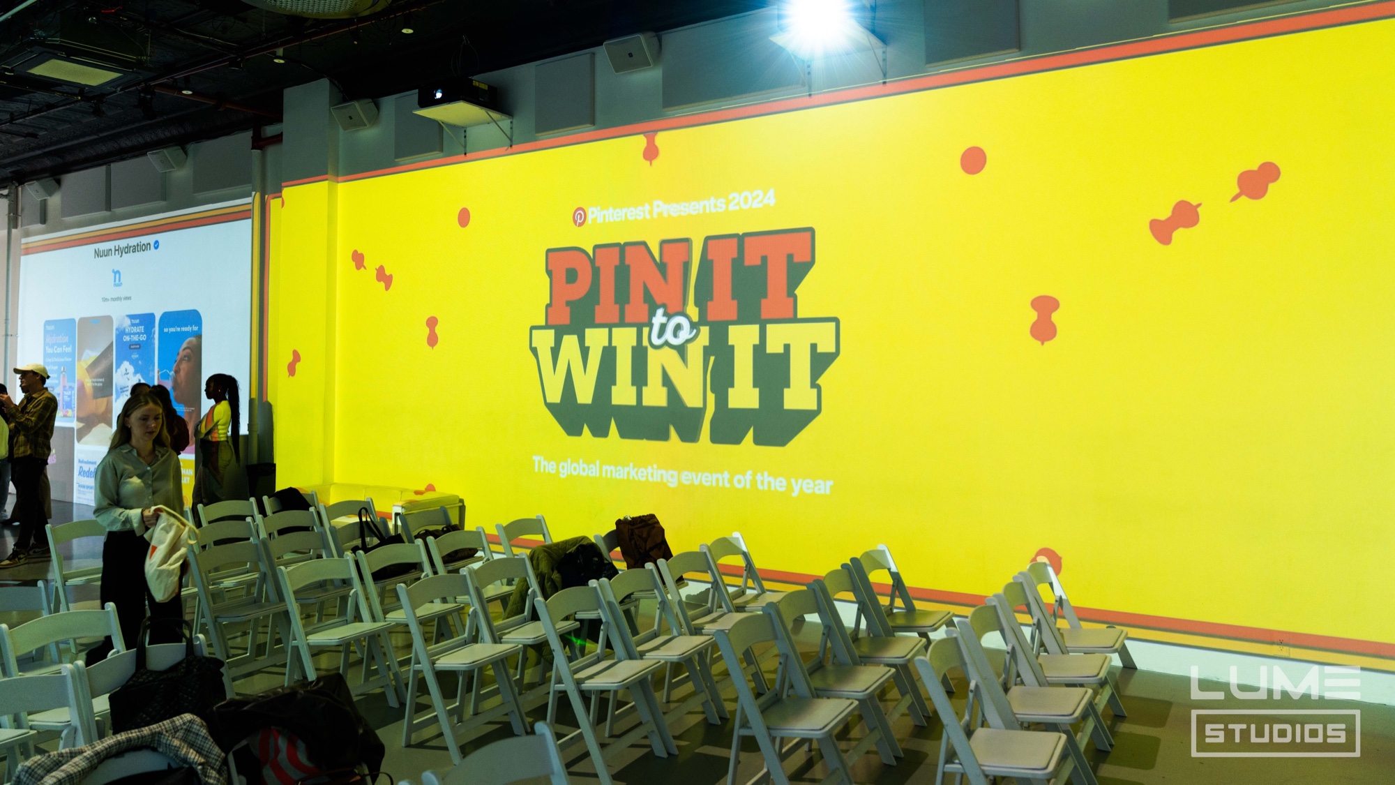 Rows of white folding chairs face the yellow Pin It to Win It projection wall