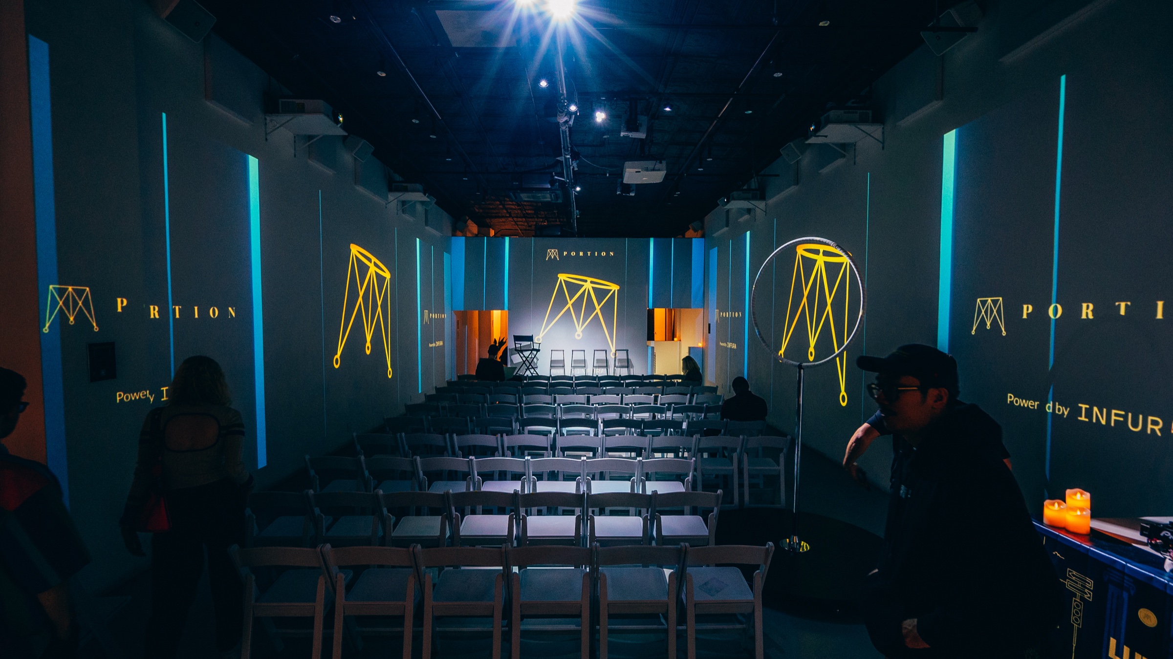 Empty rows of chairs face a stage lit blue with Portion logos projected on every wall
