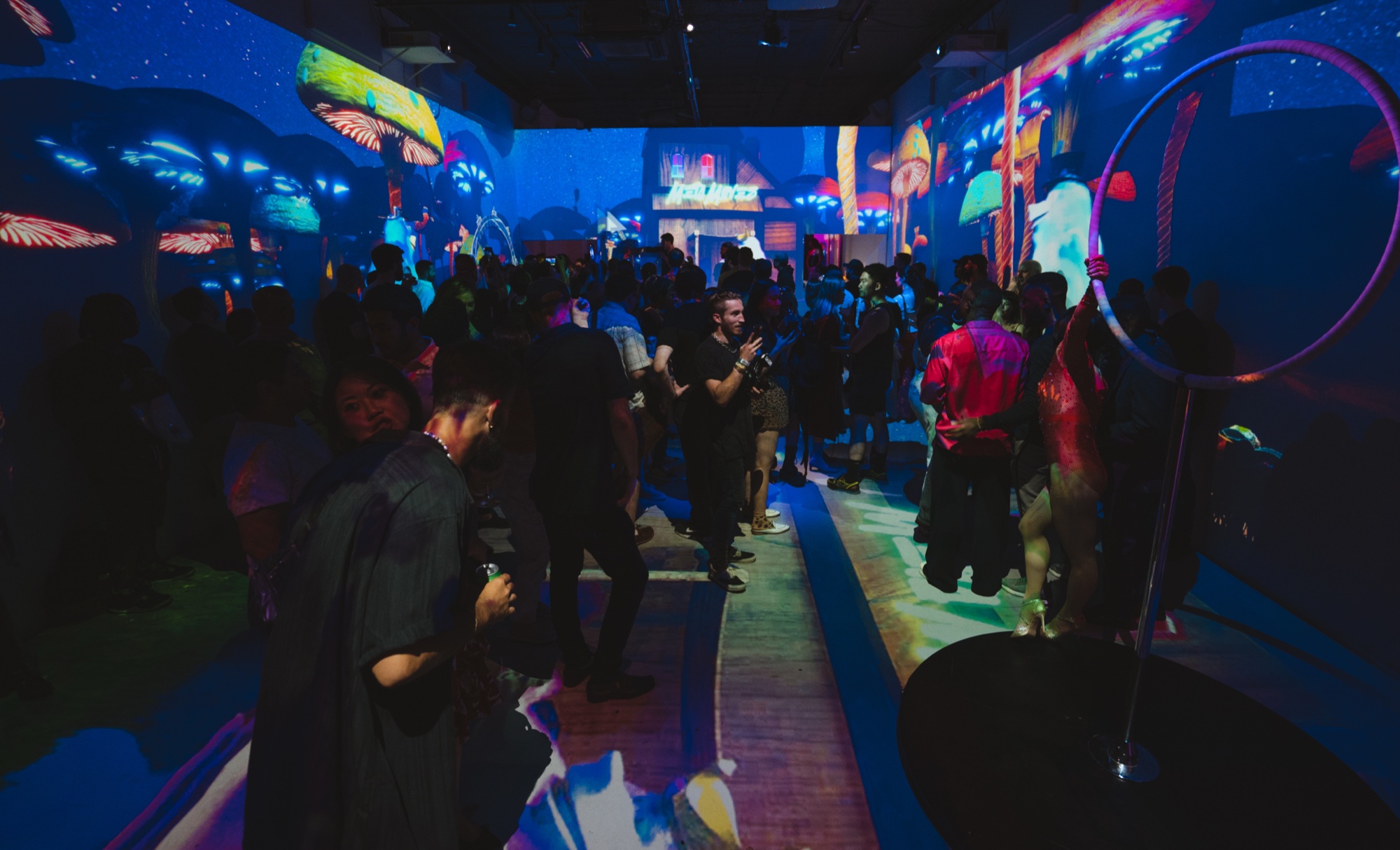 Guests mingling in a dark room lit blue by projected mushroom and forest imagery and a glowing hoop