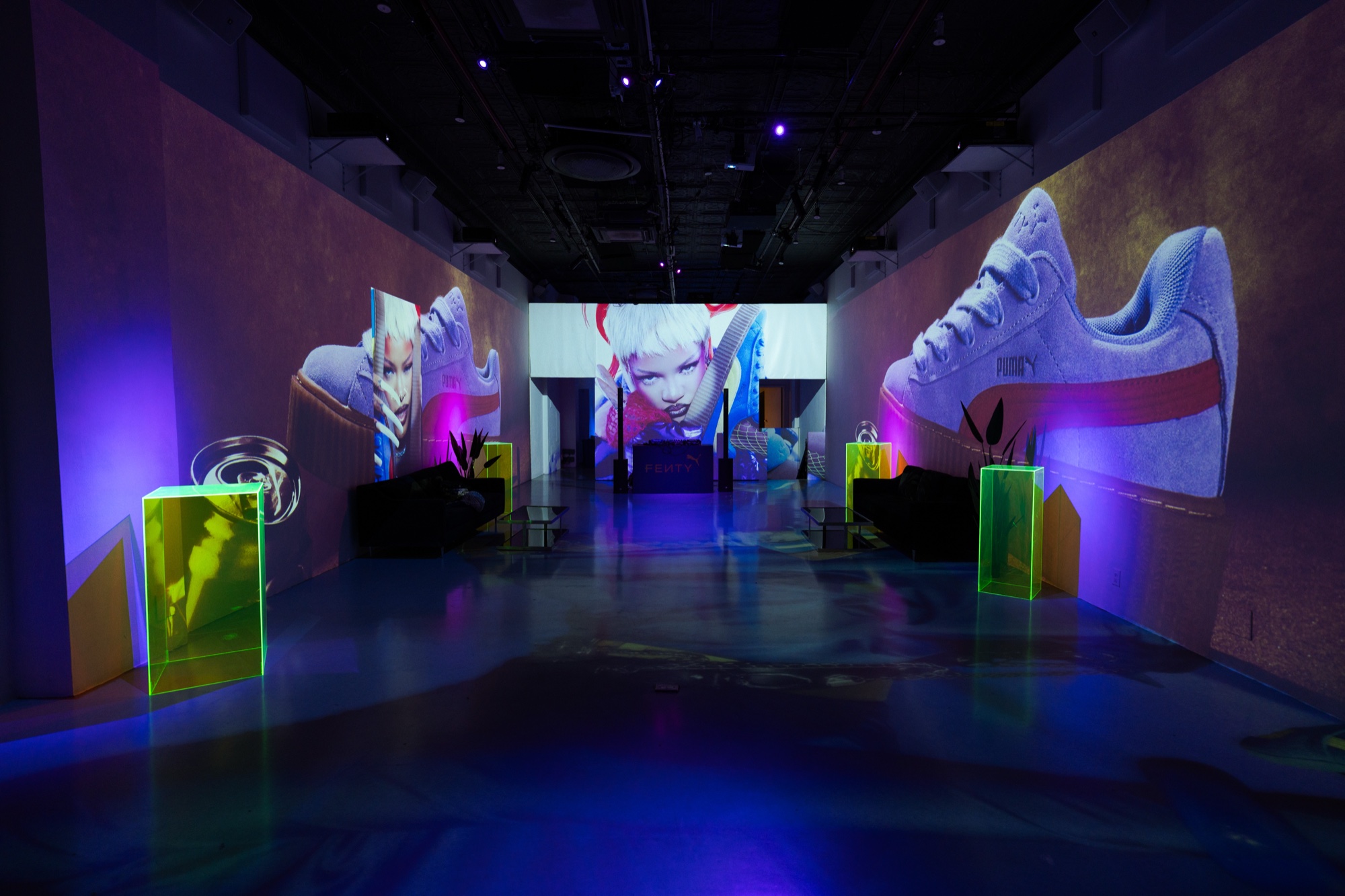 Blue lit corridor with giant projected Puma sneakers and illustrated faces, neon green acrylic boxes on the floor