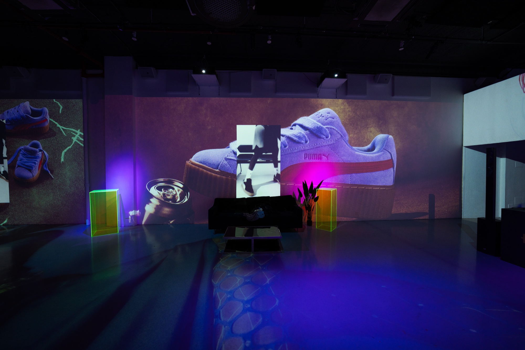 A giant Puma sneaker projected on a purple lit wall above neon green cubes and a black sofa