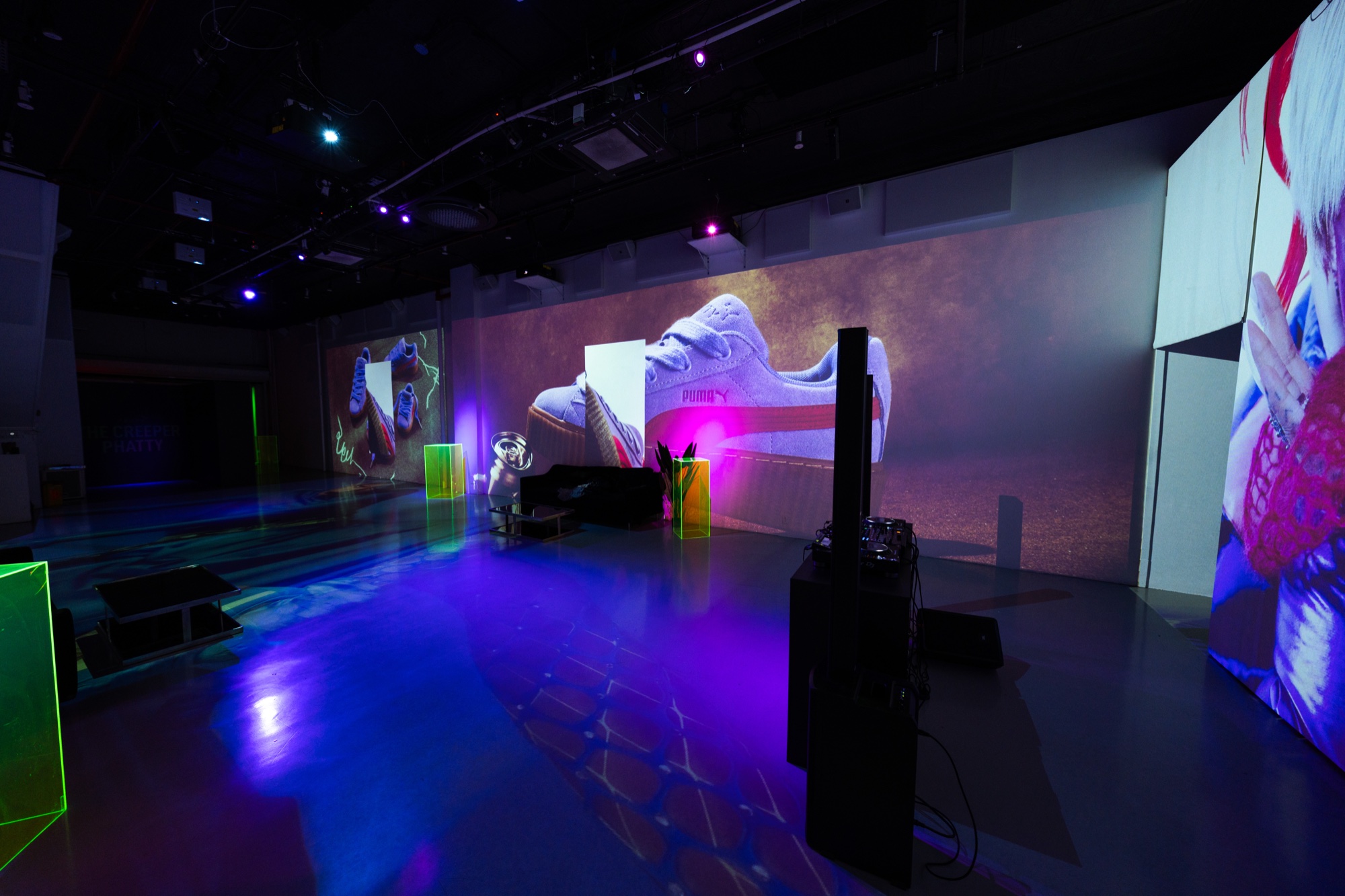 A dark studio floor glows blue and green beneath walls projected with a giant white sneaker and portrait imagery