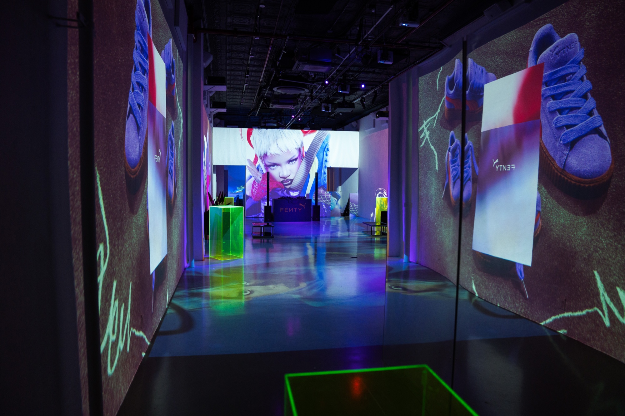 Blue suede Puma sneakers projected on both walls of a corridor leading to a screen with a white haired portrait