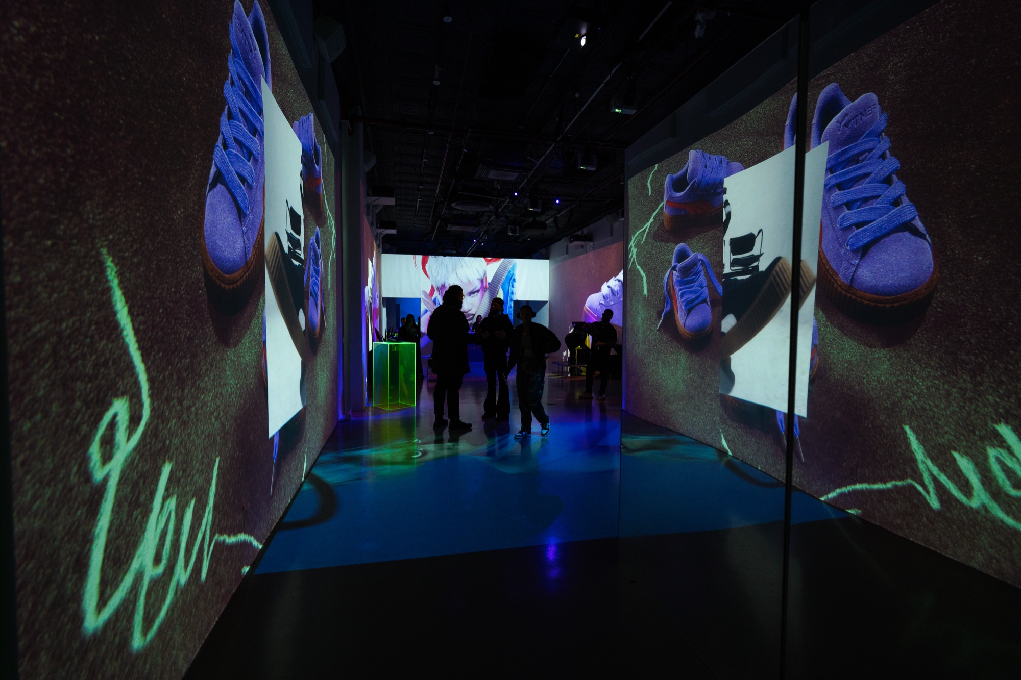 Visitors silhouetted in a hallway with projected purple sneakers and green graffiti scrawled on both walls
