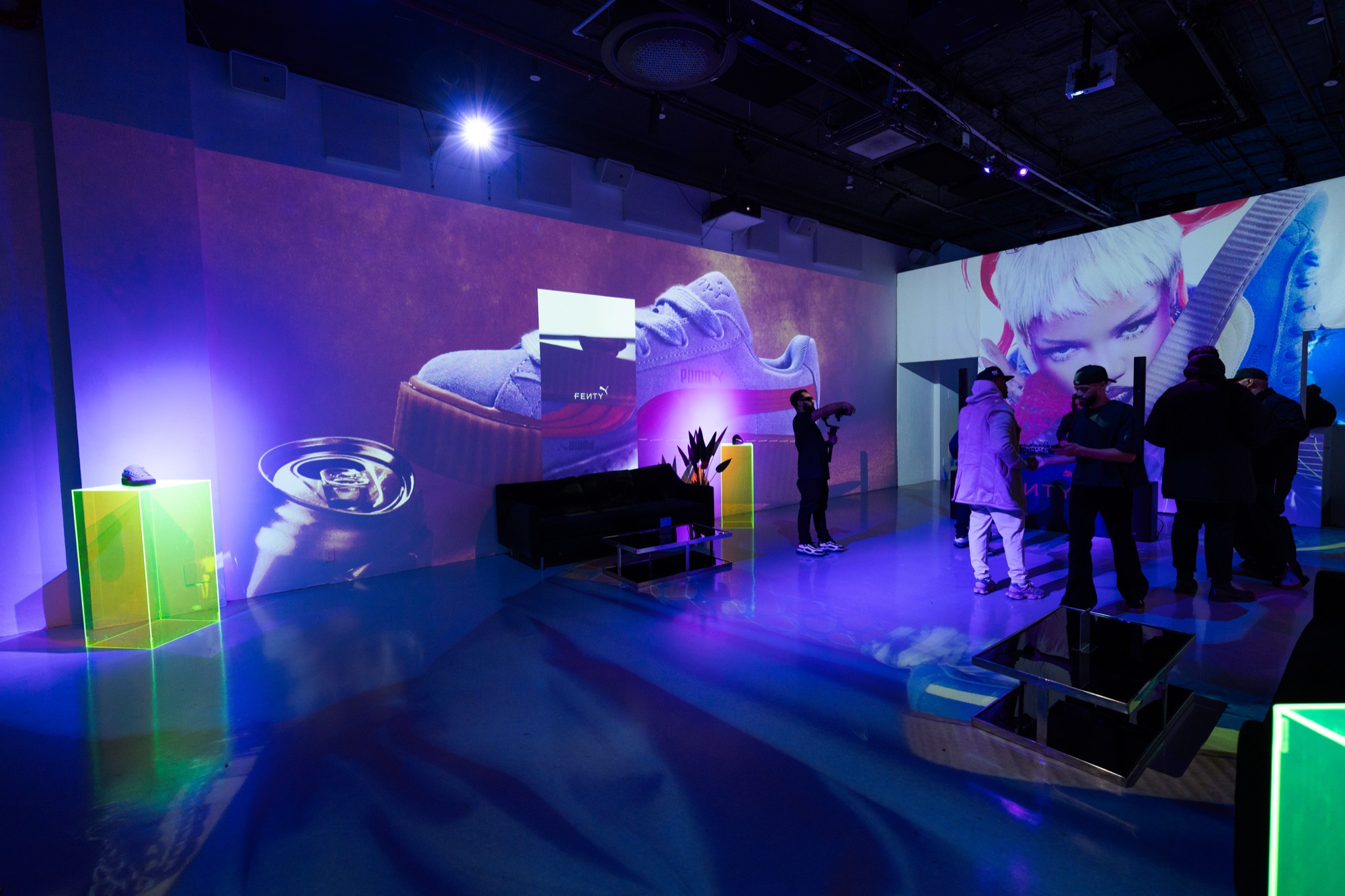 Guests stand in a purple lit room with a giant sneaker and a white haired face projected on the walls