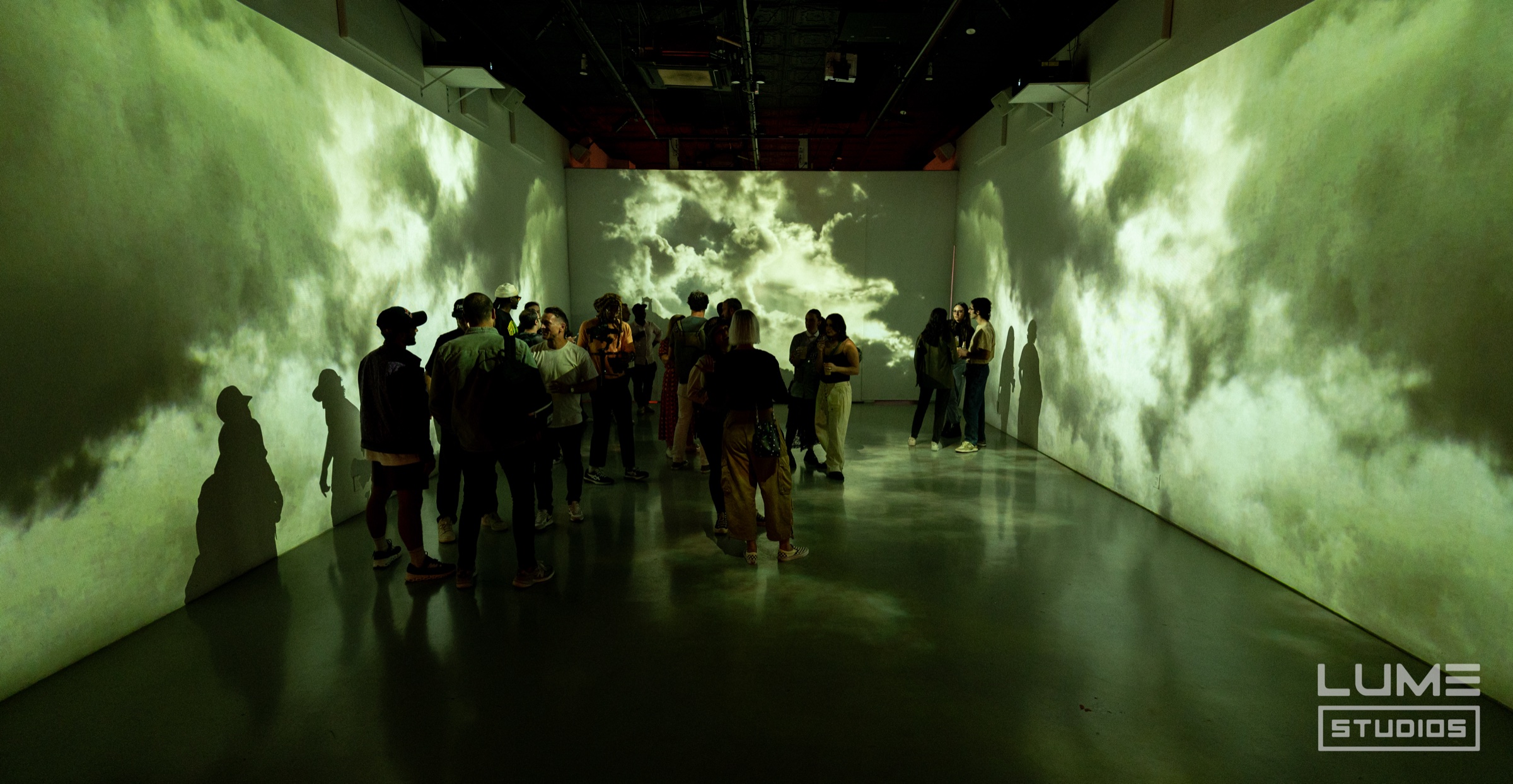 Guests stand in a dark room whose walls are projected with swirling green tinted clouds of dust