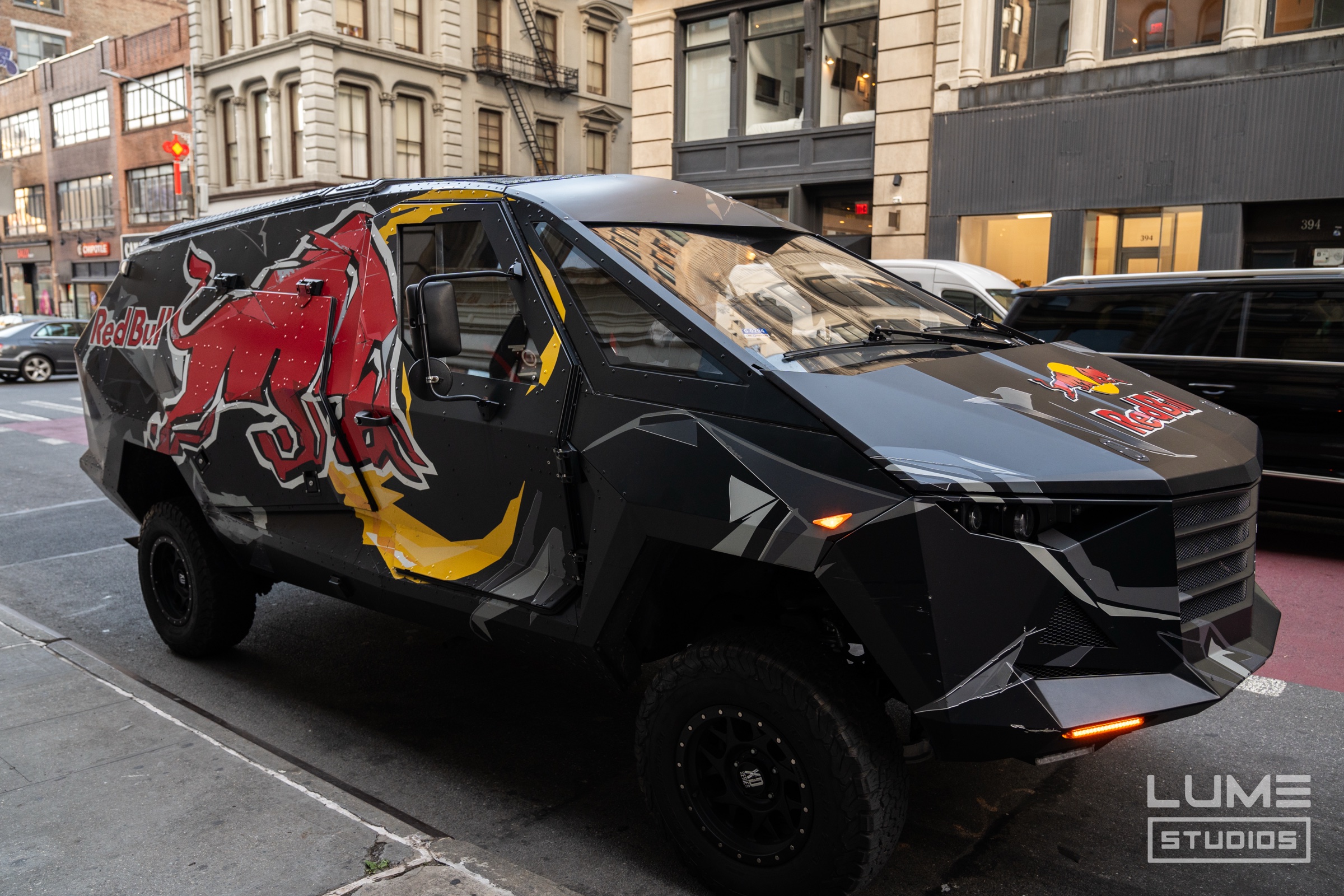 Black angular off road van with a red charging bull and Red Bull logo parked on a city street