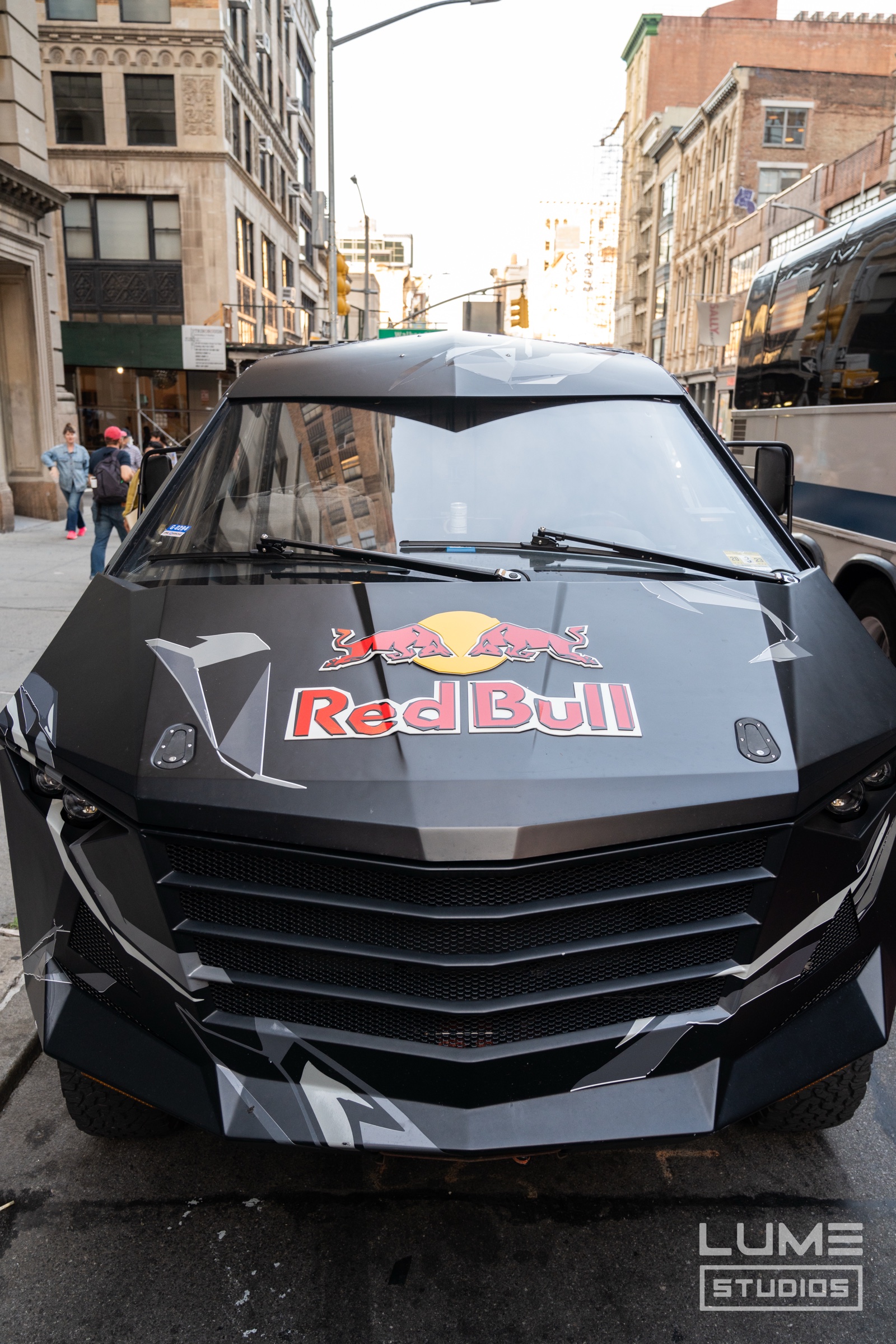 Matte black armoured van with a Red Bull logo on its hood parked on a city street