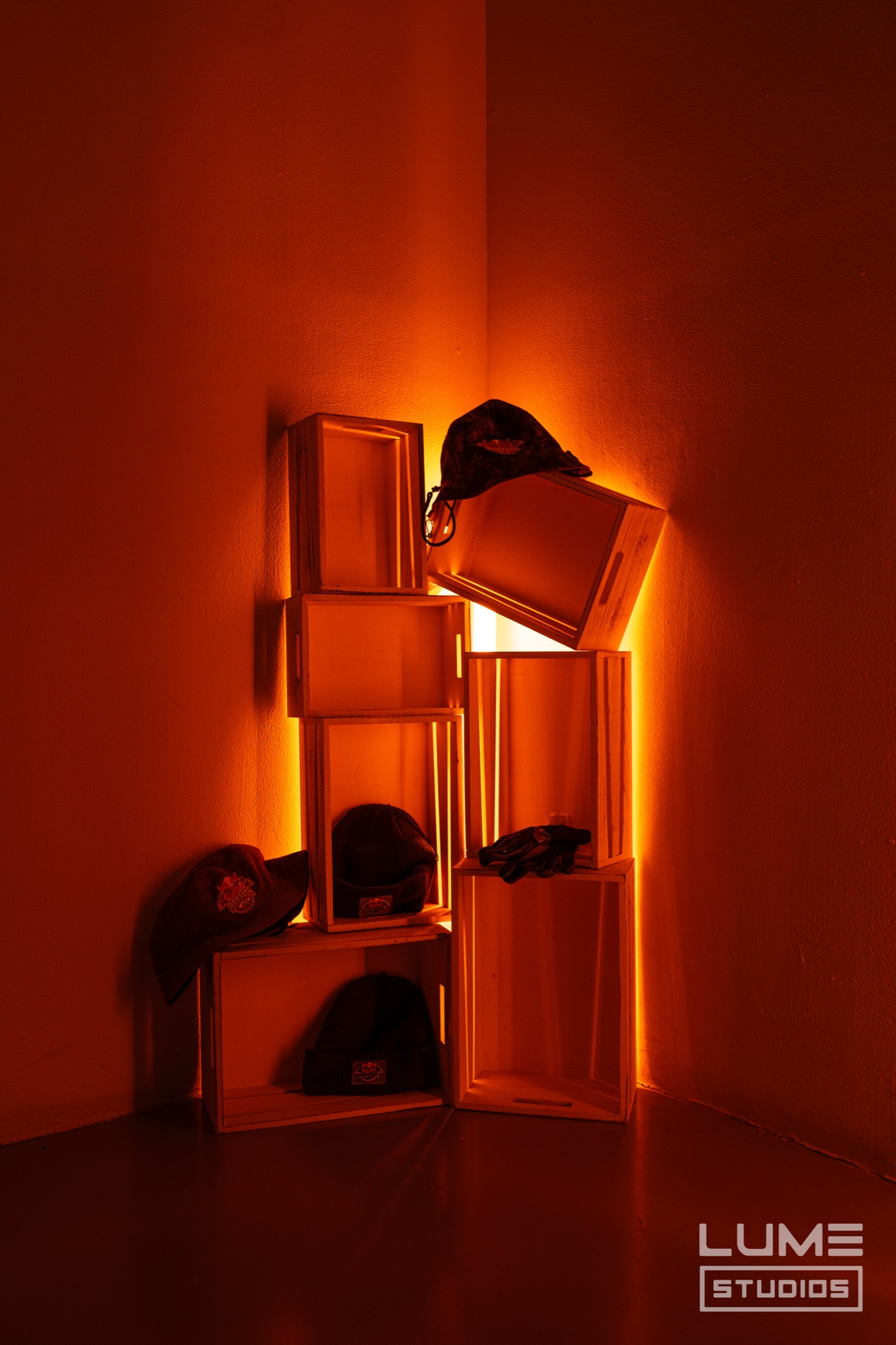 Stacked wooden crates holding caps and gloves in a corner washed in deep orange light