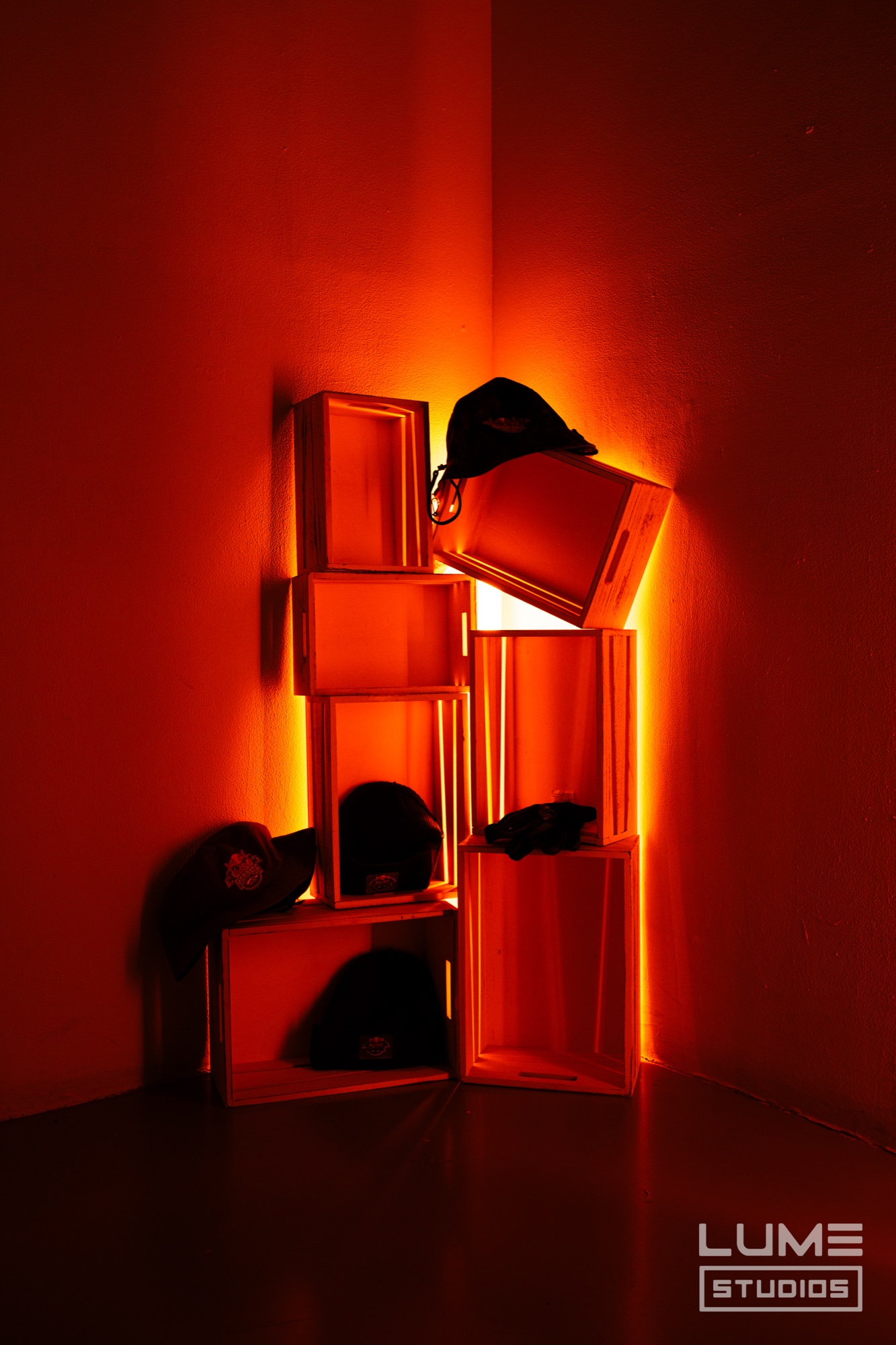 Stack of wooden crates holding black caps lit from within in a corner washed in orange light