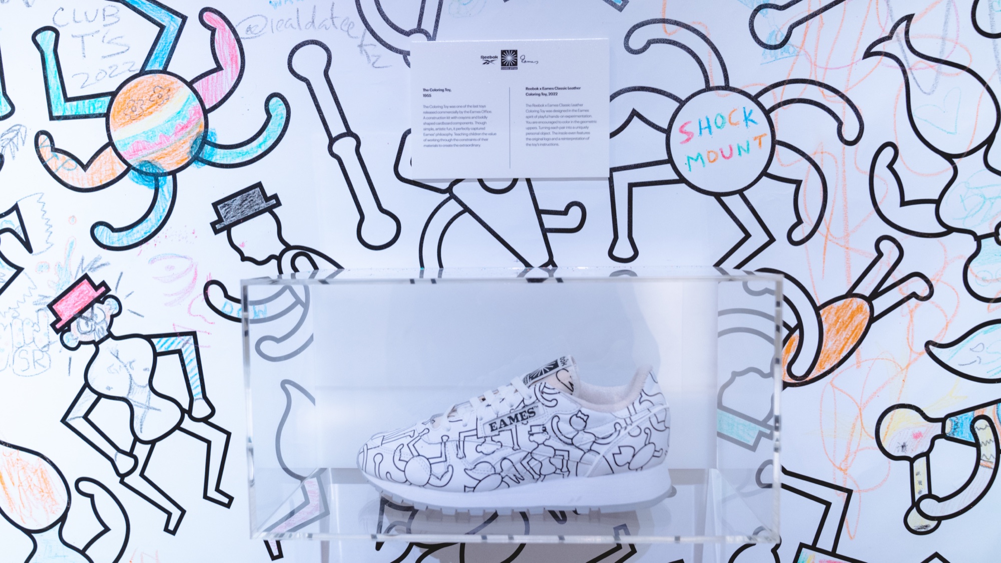 White sneaker covered in black line drawings in a lit case against a wall of dancing line figures