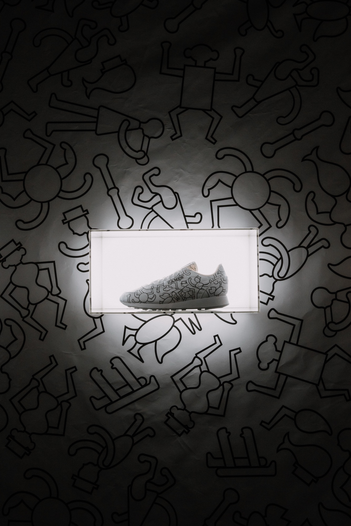 Doodled white sneaker in a glowing acrylic box on a dark wall covered with outline figures