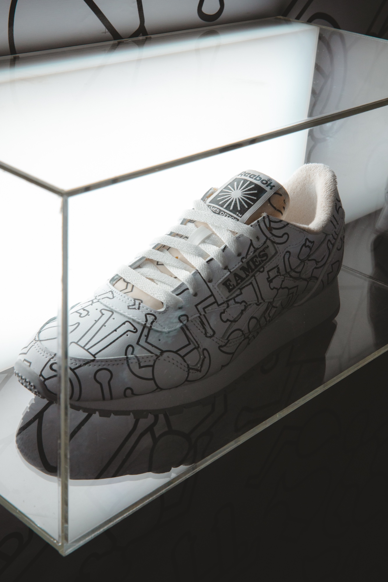 Close up of a white Reebok sneaker printed with black line figures and an Eames tongue label