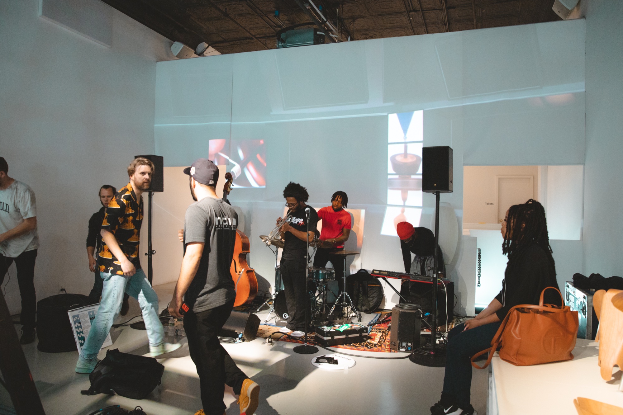 Band with an upright bass and keyboards sets up in a white room as guests walk past