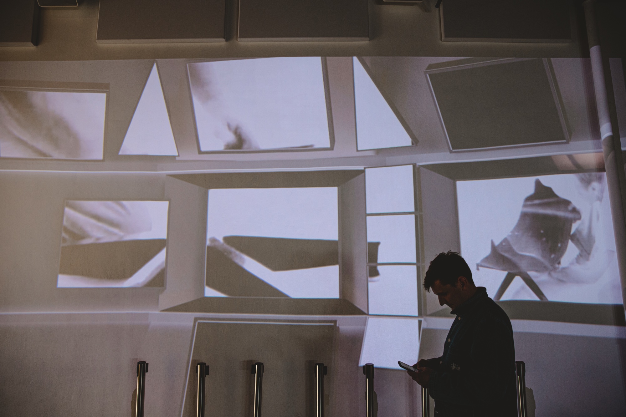 Silhouetted man on his phone before a wall of tilted projected panels showing black and white photographs