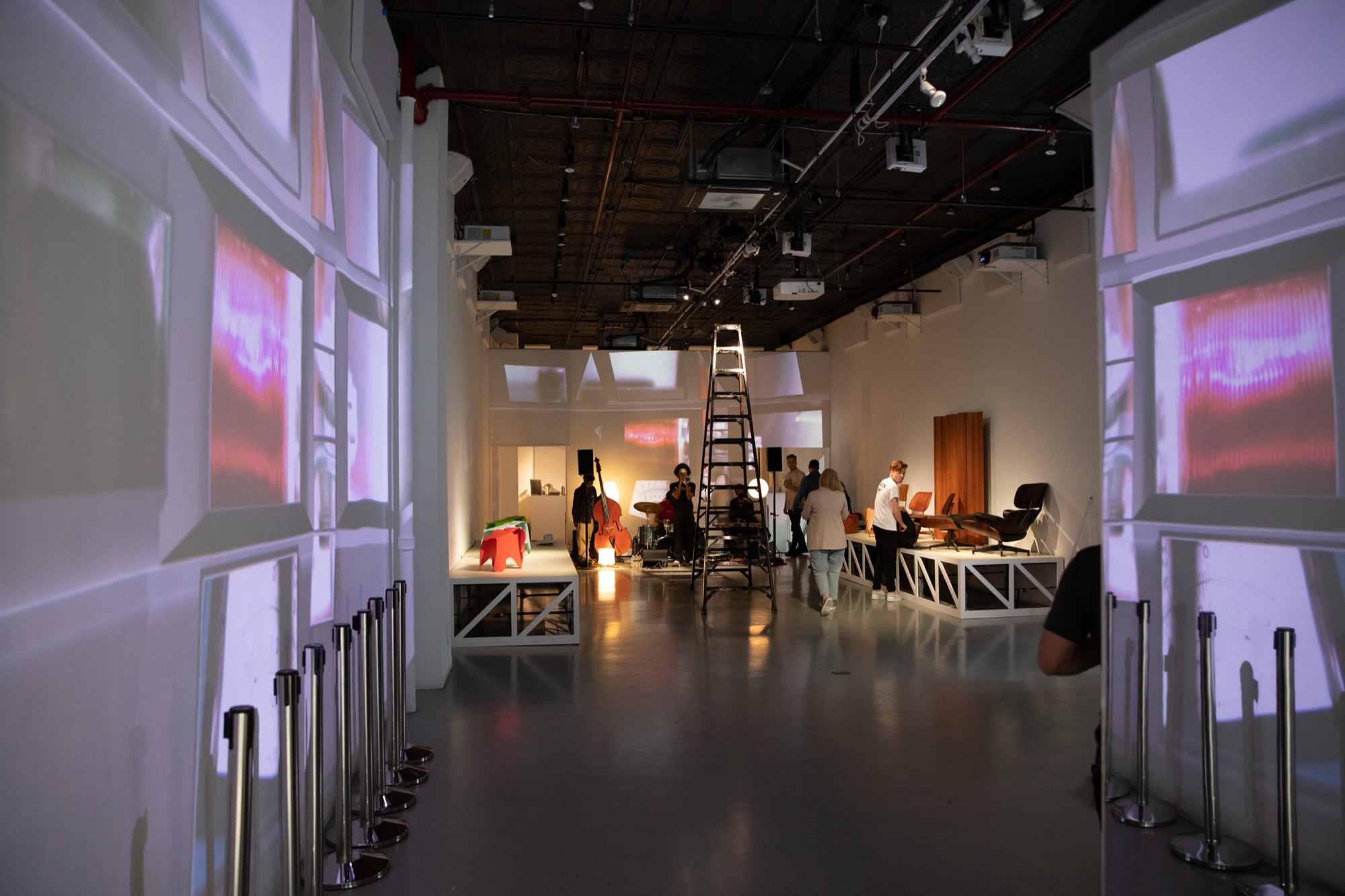Gallery corridor lined with projected panels and stanchions leading to a ladder and people setting up