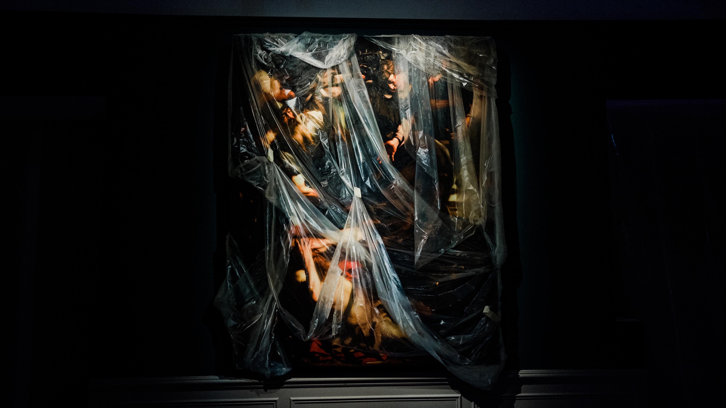 Robin Eley painting draped in translucent plastic glows under a single spotlight in a dark room