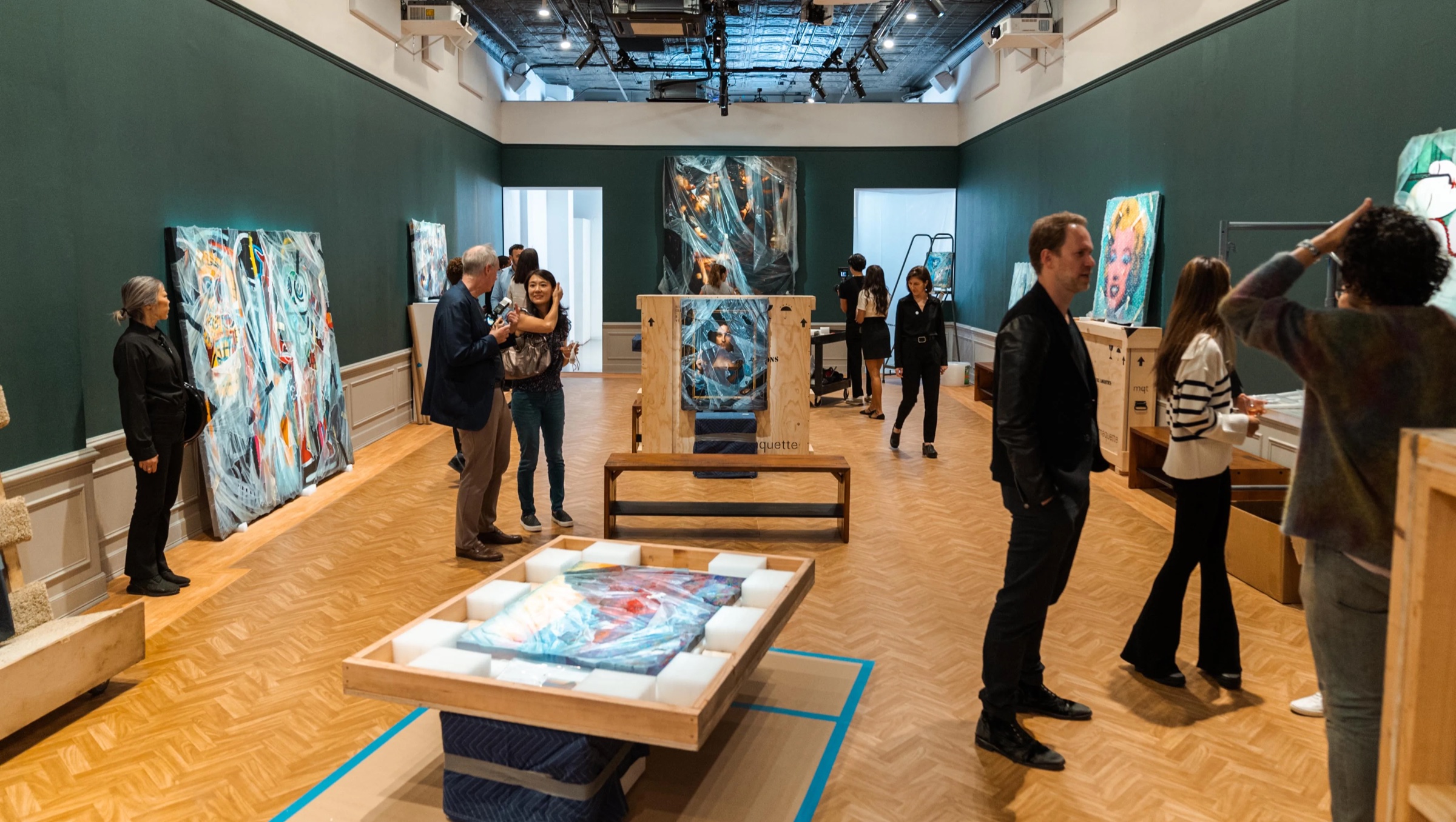 Visitors examine wrapped paintings in a green walled gallery at the Robin Eley exhibition