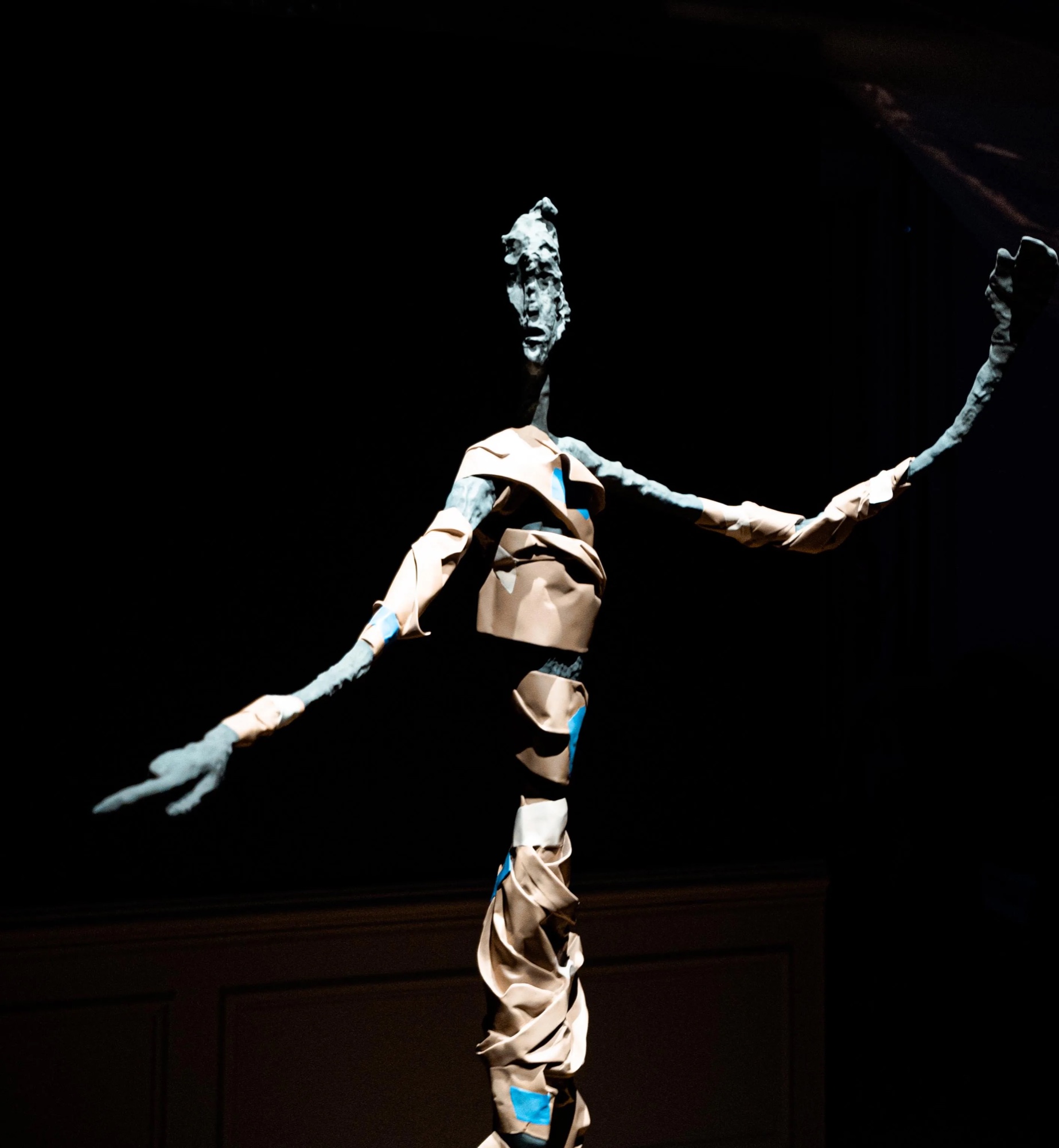 Tall sculpted figure with outstretched arms lit against darkness at Robin Eley