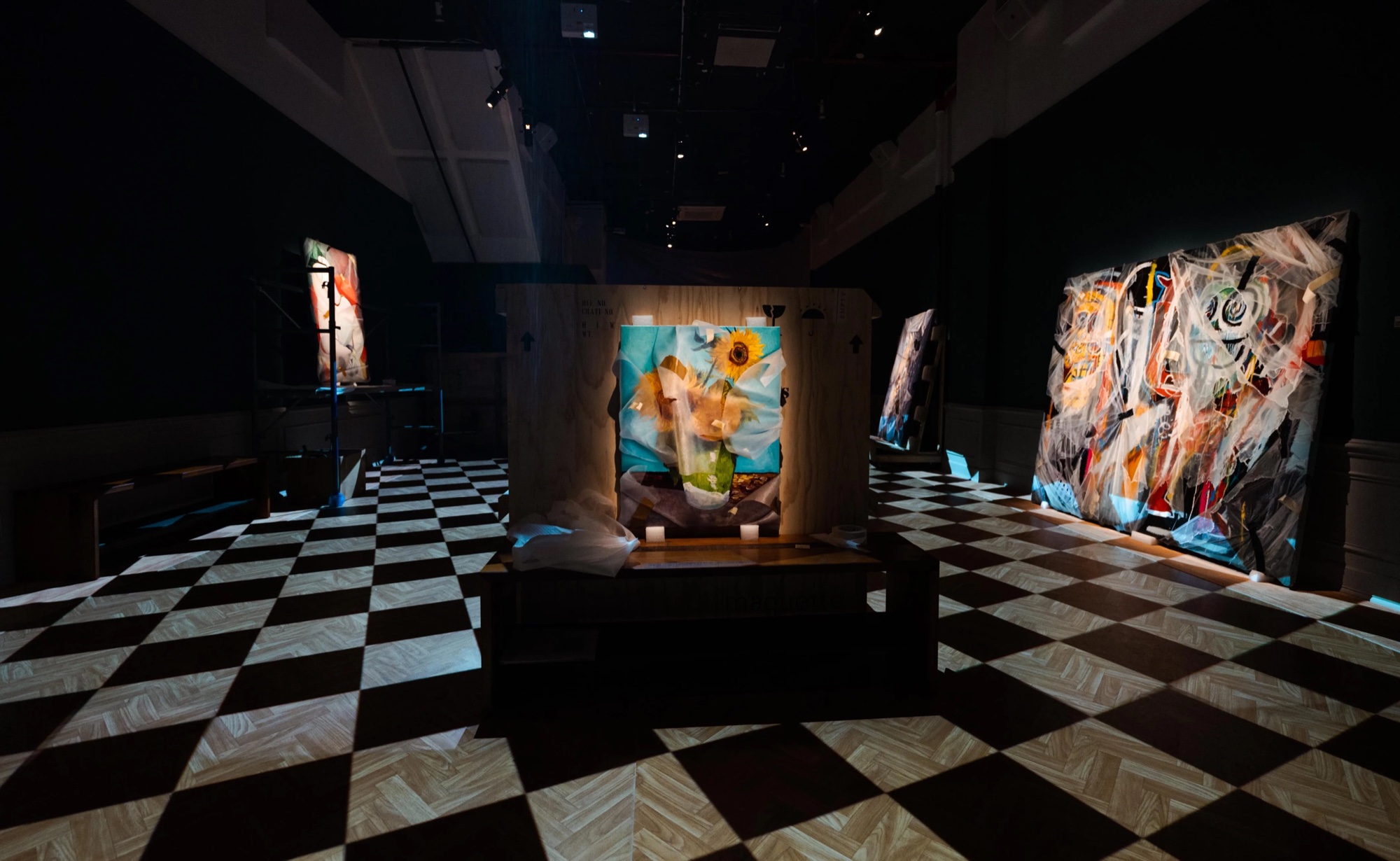 Dim gallery with a checkerboard floor and wrapped paintings on scaffolding