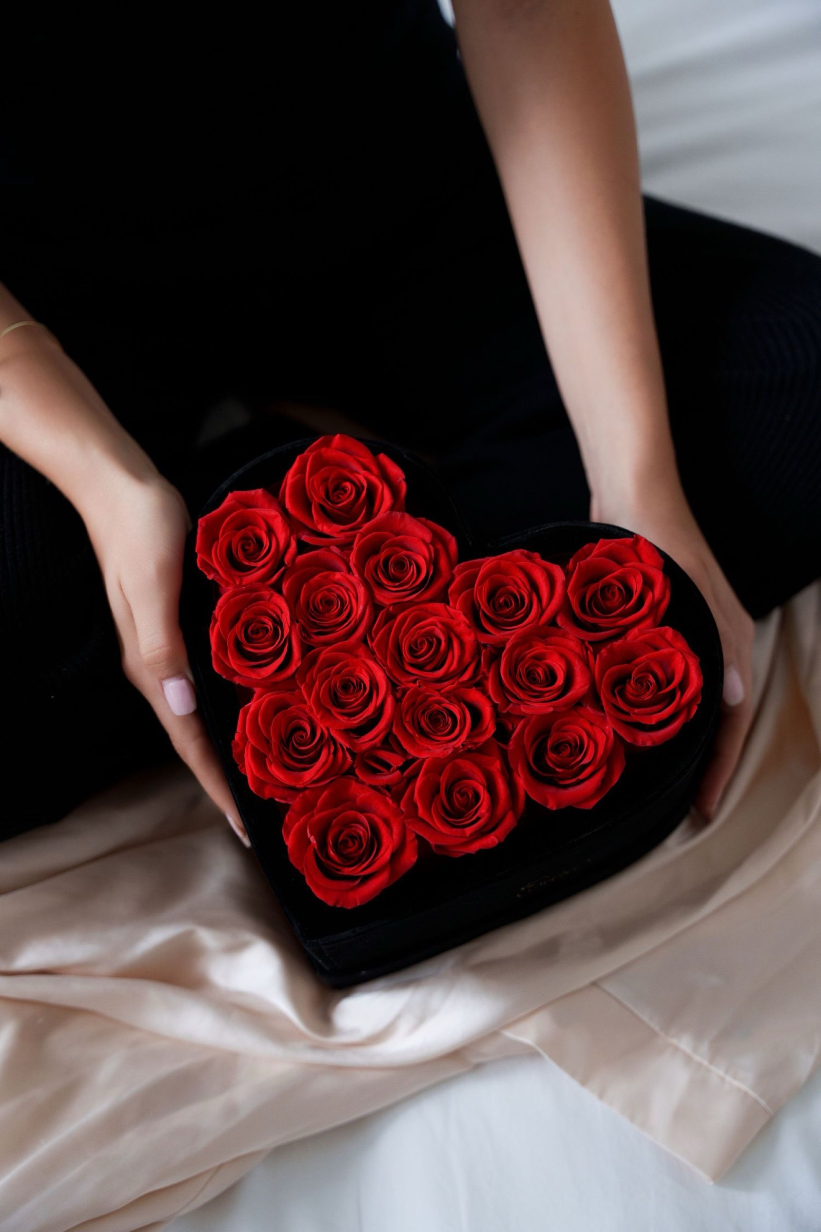 Woman in black holds a box shaped like a heart and filled with red Rose Forever roses