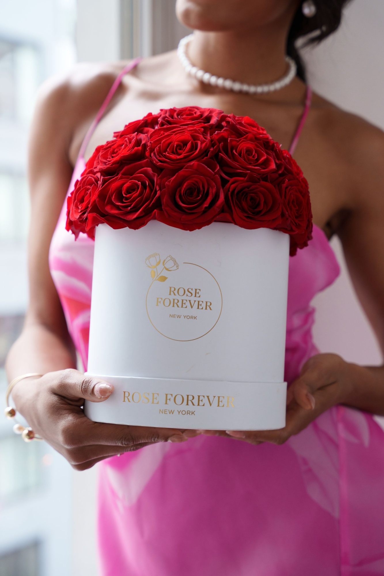 Model in pink holds a white Rose Forever New York hatbox topped with red roses