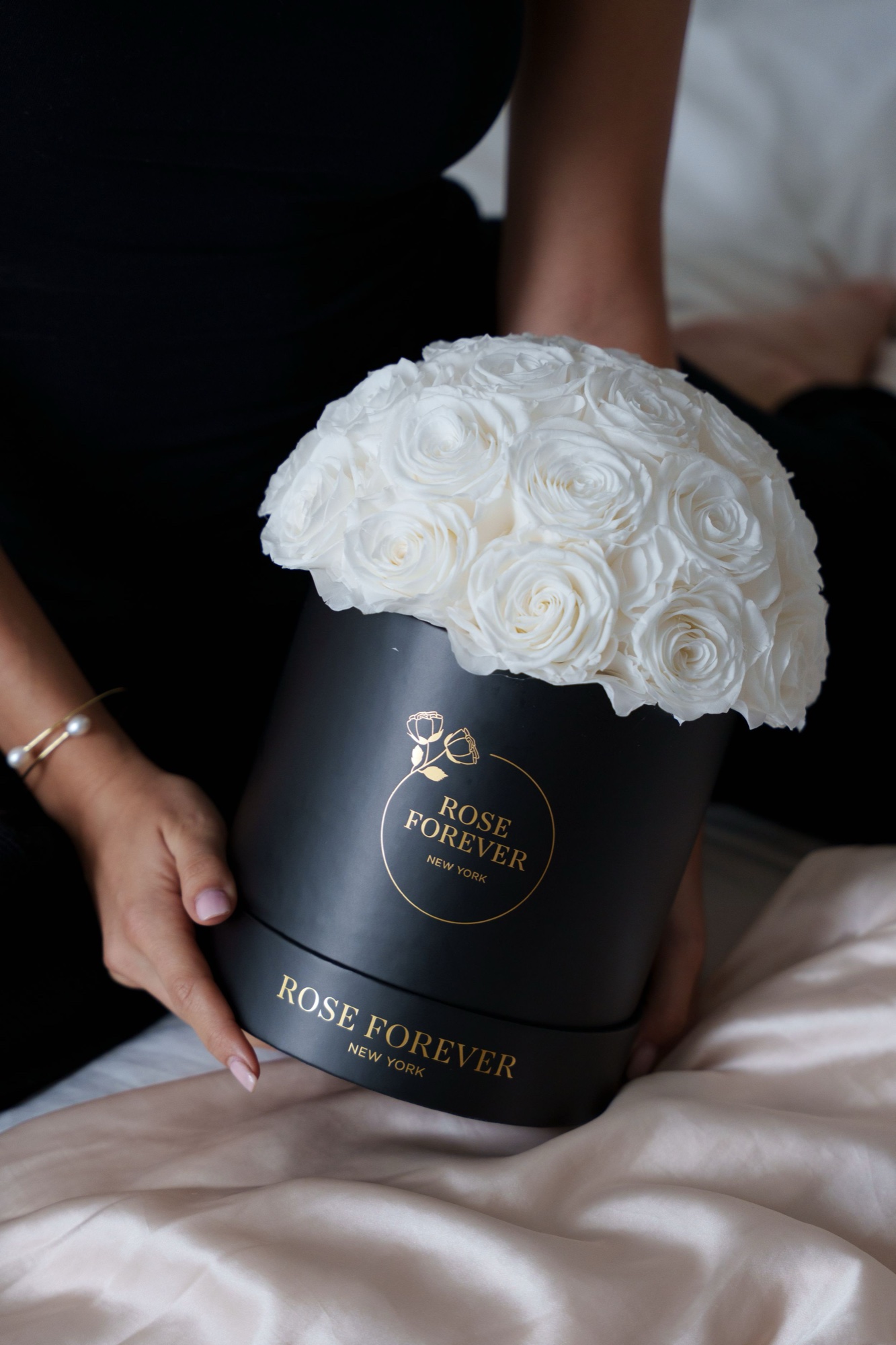 Hands steady a black Rose Forever box crowned with a dome of white roses