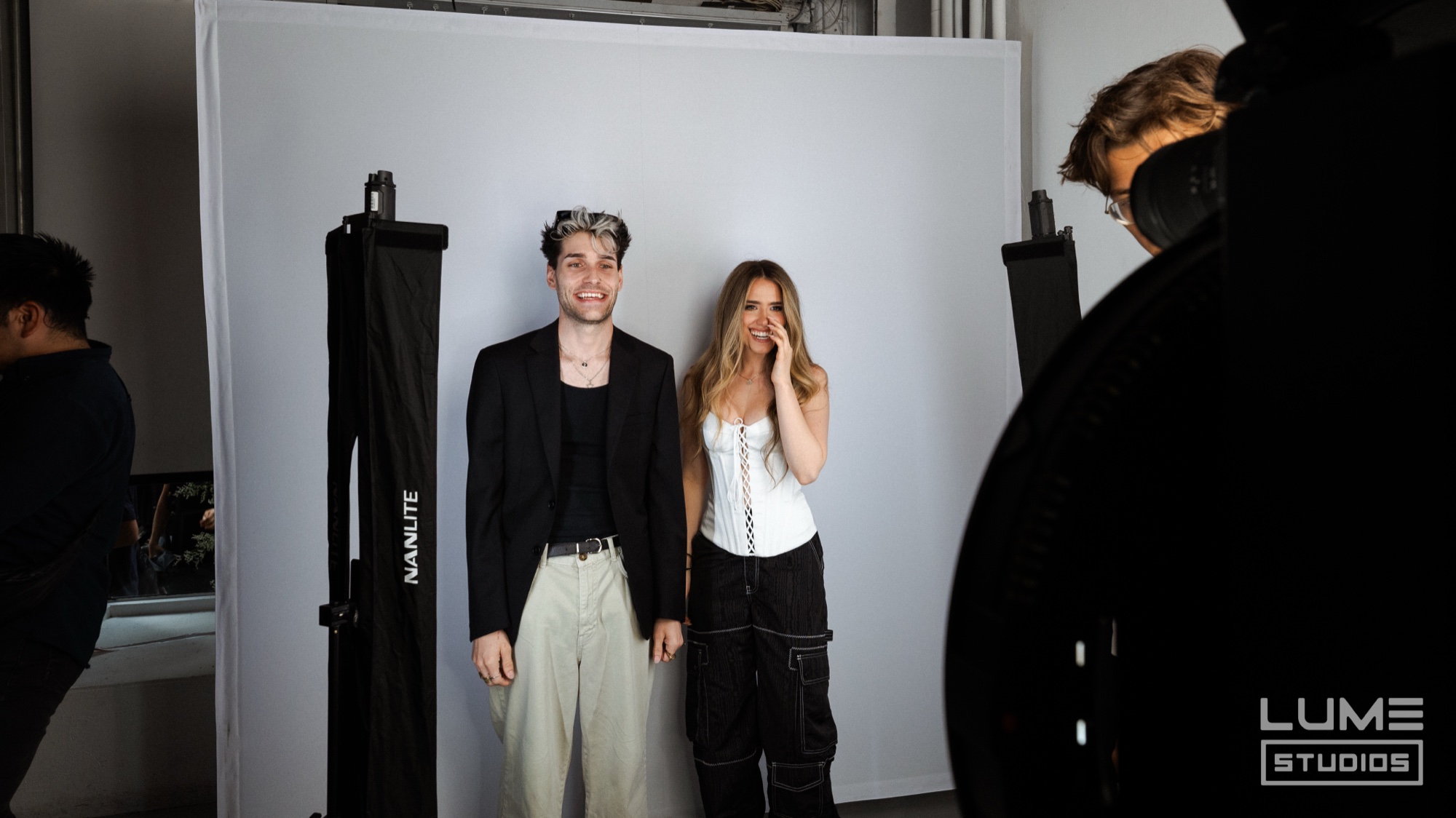 Pair pose on a white photo backdrop flanked by tall softboxes while a photographer stands at right