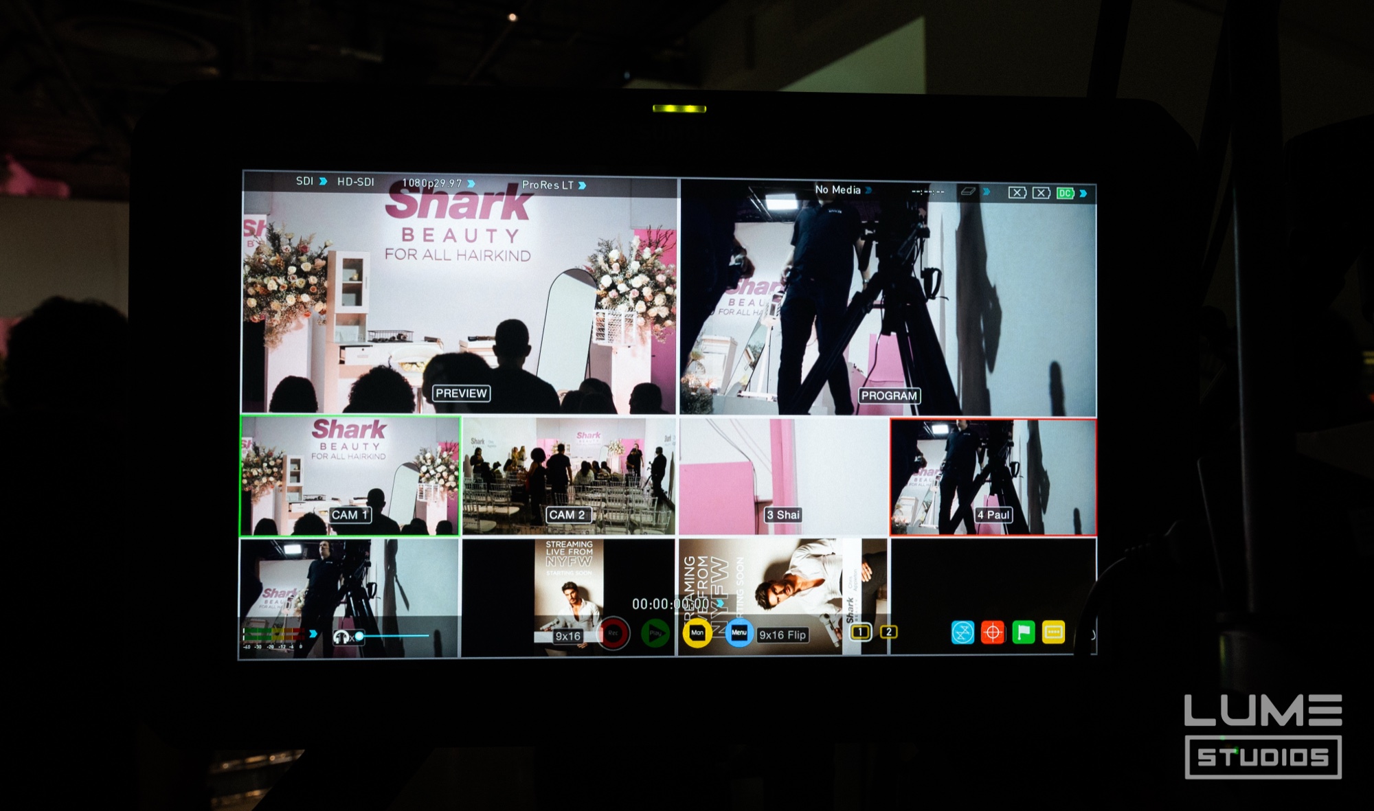 Multiview video monitor showing camera feeds of a Shark Beauty stage with white flowers and a crowd