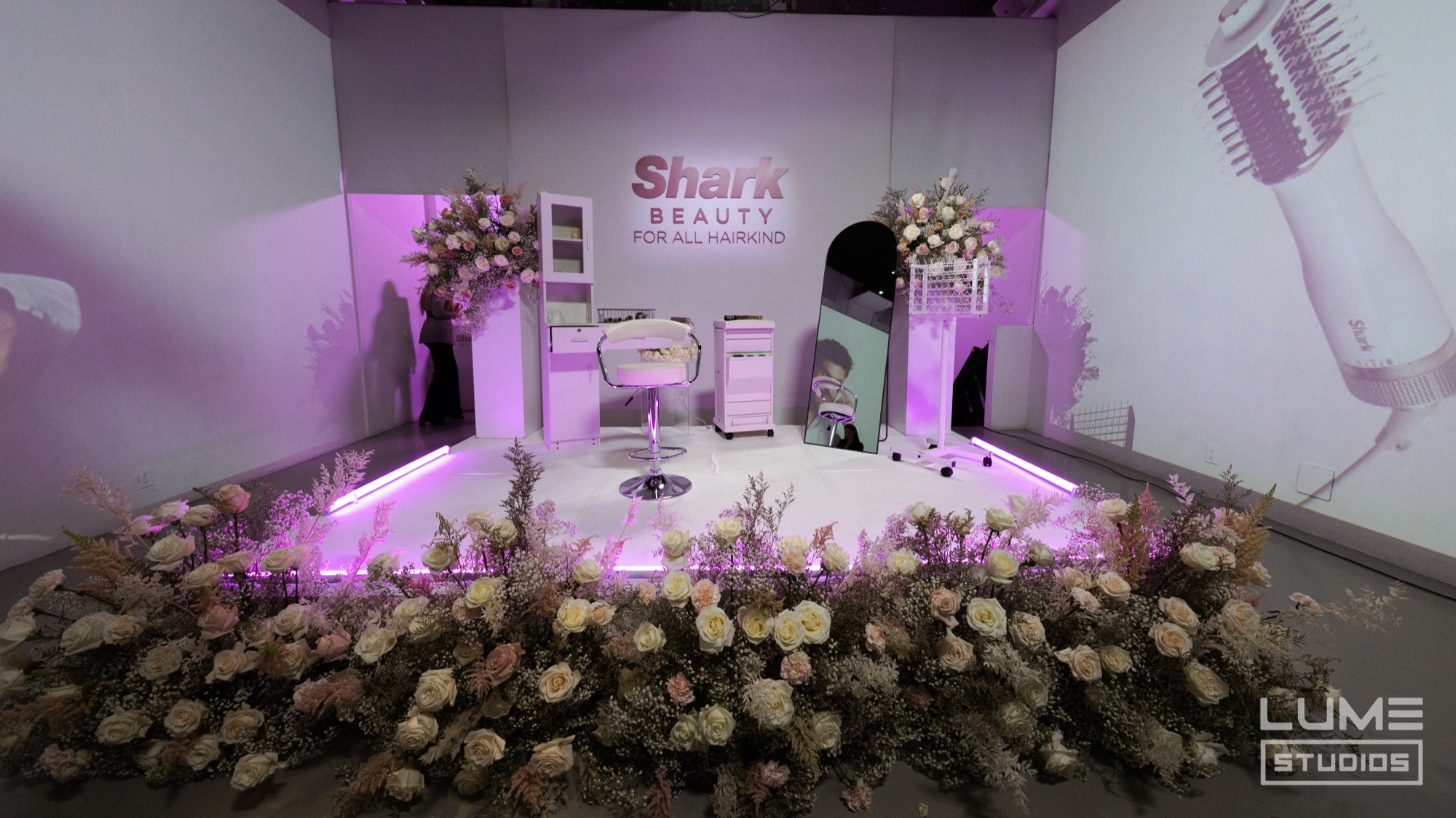 Shark Beauty stage with a white salon chair, pink roses and a projected hair styling tool
