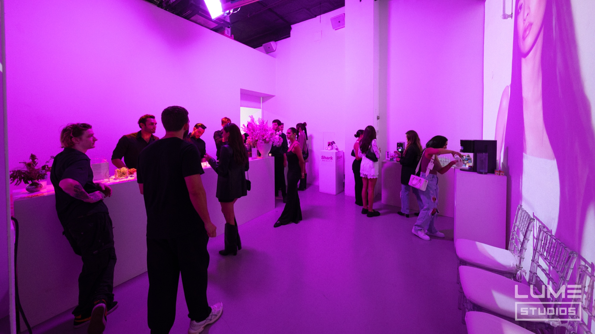 Guests mingle in a room washed in magenta light with a giant face on the wall at right