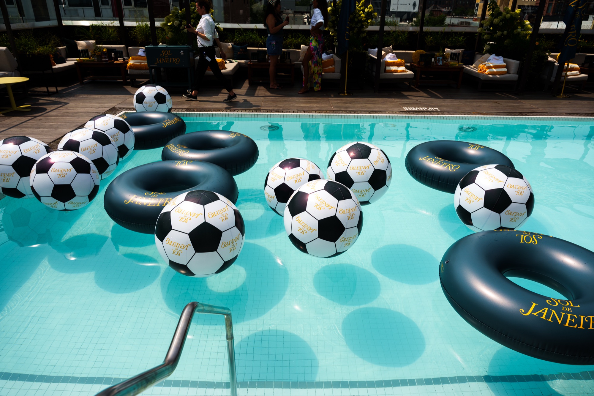 Black and white soccer ball floats and dark green rings drift in a rooftop pool with lounge chairs beyond