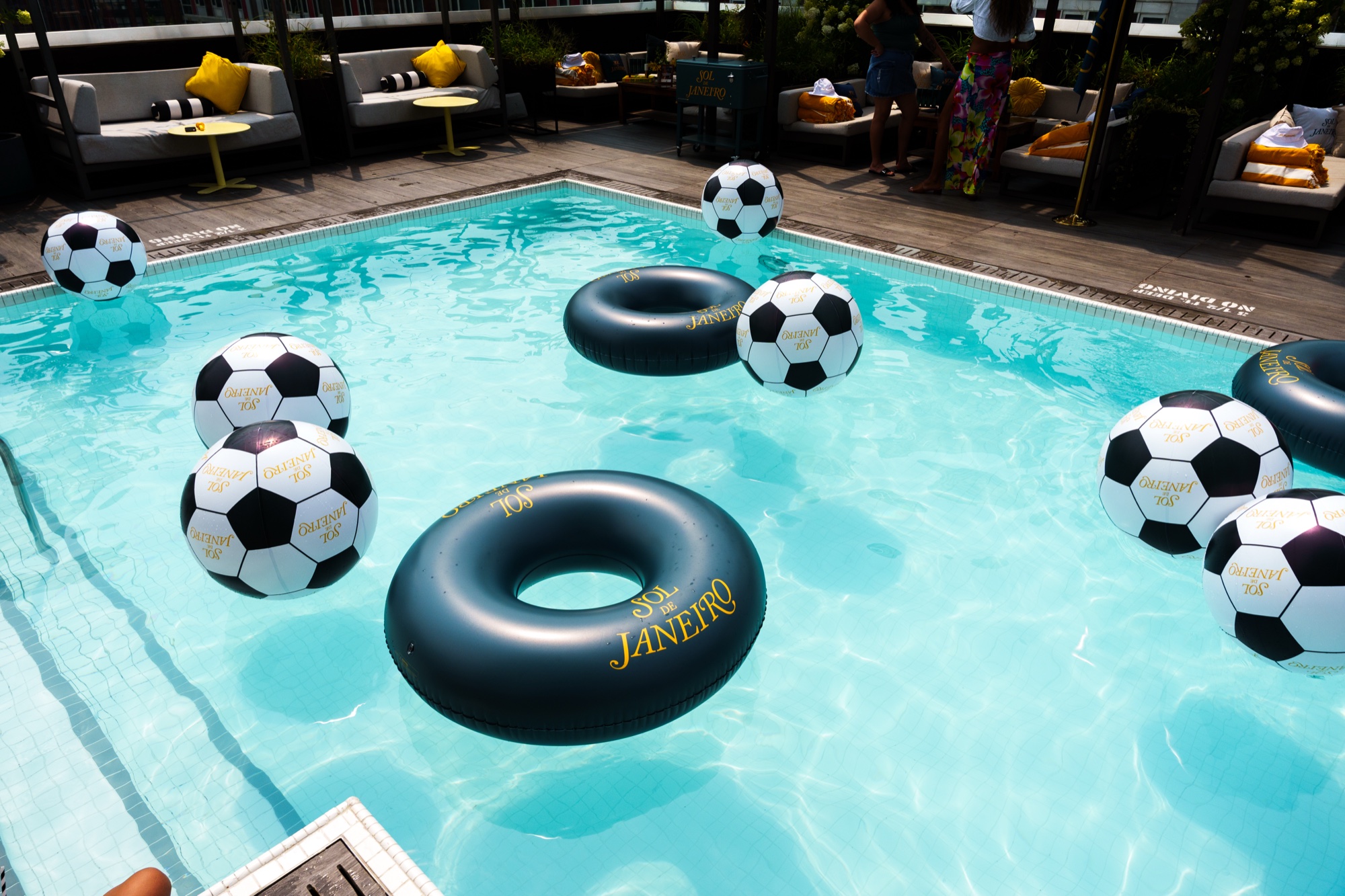 Rooftop pool scattered with soccer ball floats and black Sol de Janeiro rings beside white cabanas