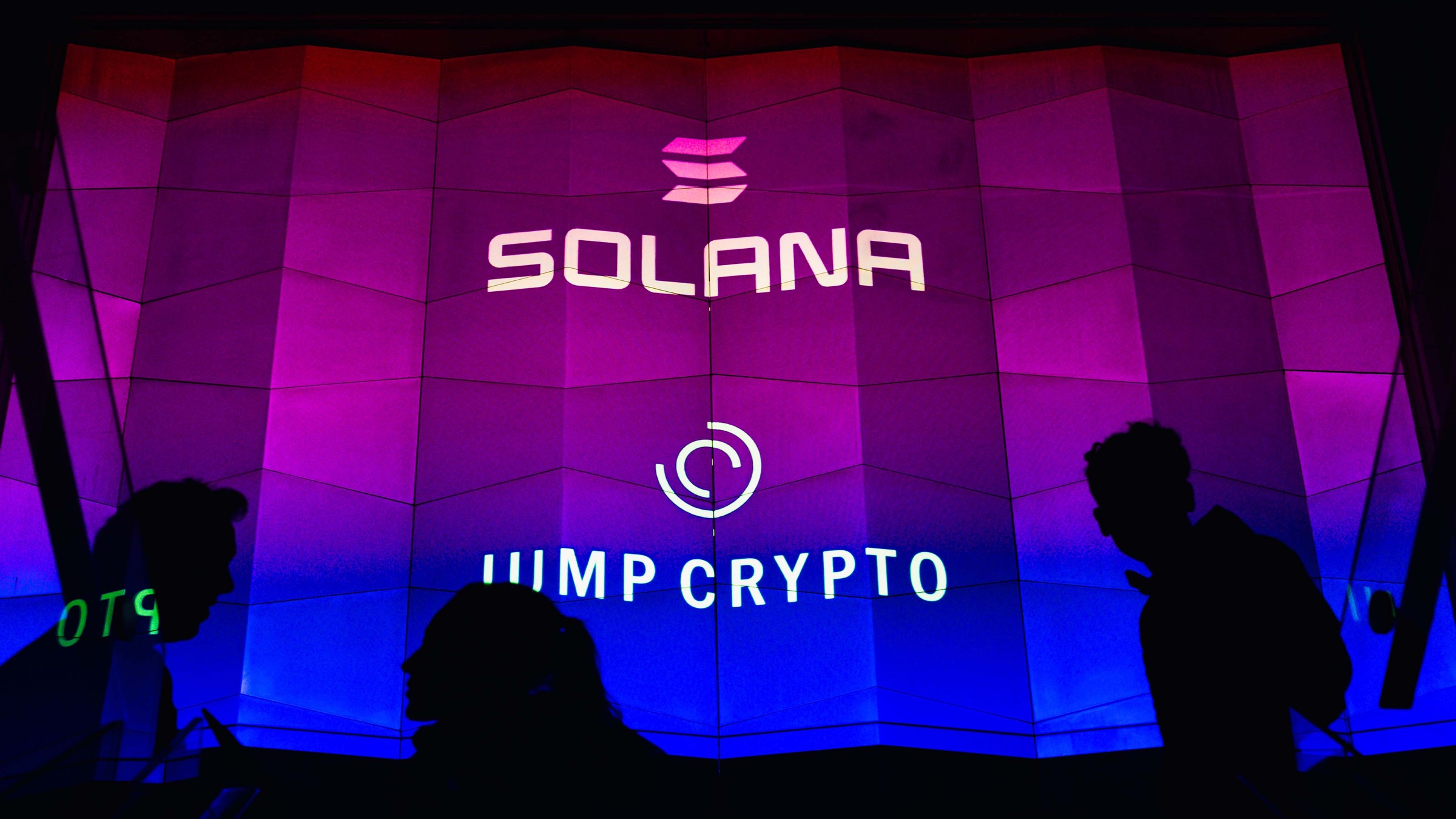 Silhouetted guests before a glowing Solana and Jump Crypto wall in pink and blue