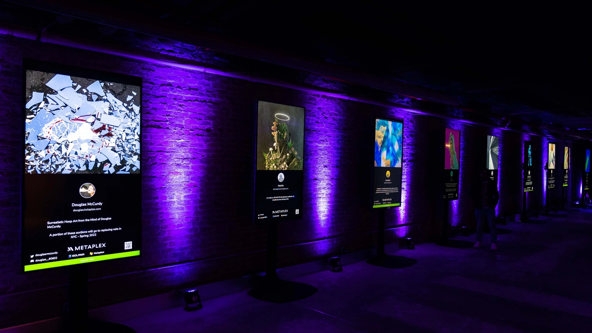 Row of lit artwork panels along a brick wall in violet light at the Solana bootcamp