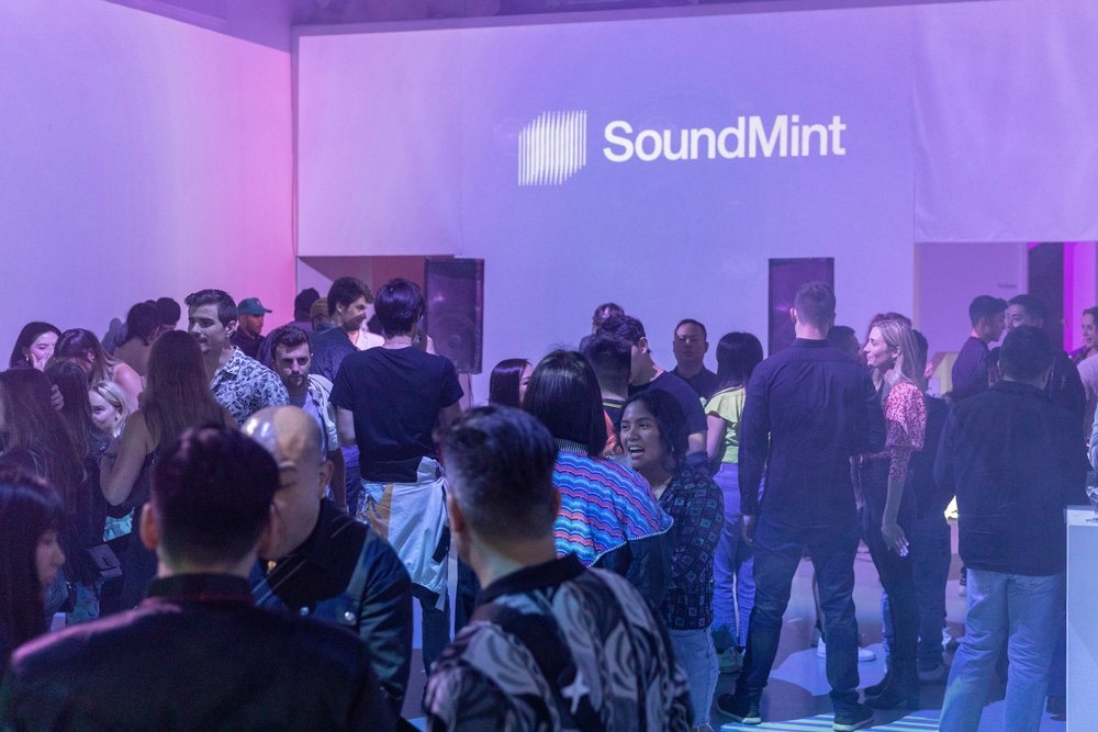 Party guests fill a room lit in violet beneath a large projected SoundMint logo