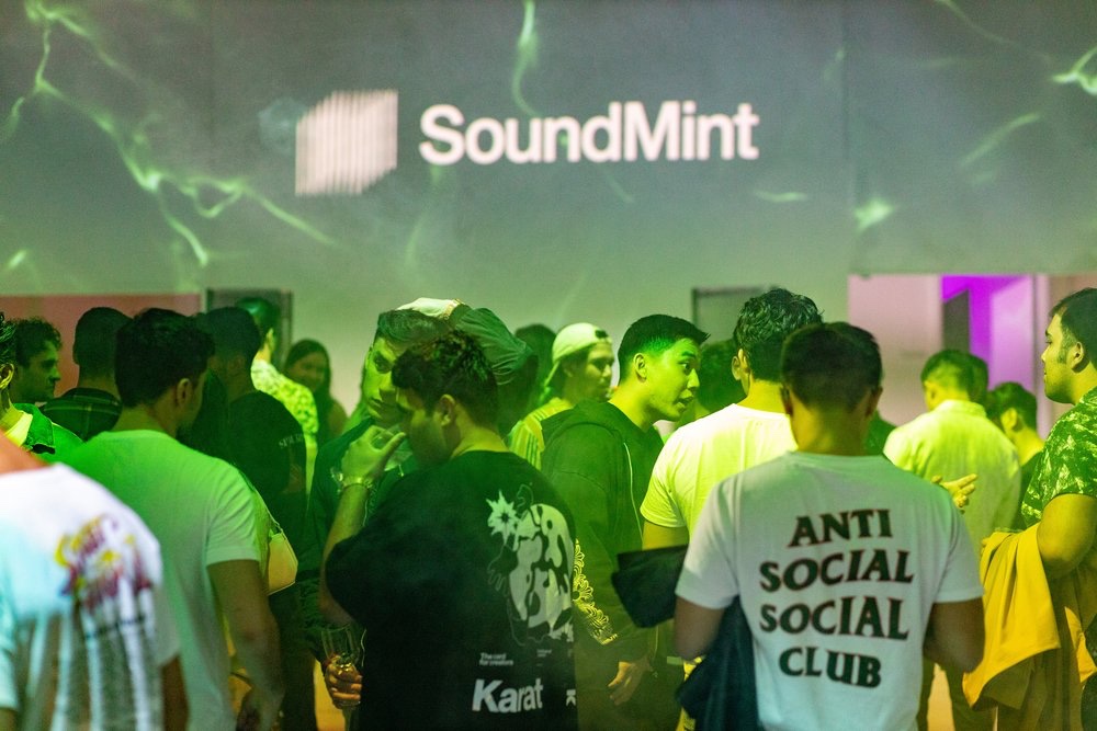 Crowd talks under green light and a SoundMint logo, with one shirt reading Anti Social Social Club