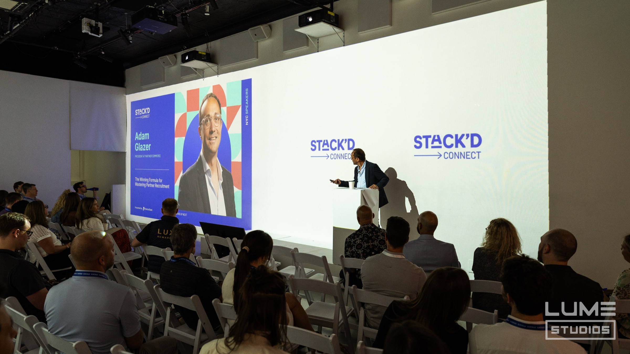 Attendees network among white chairs as bold geometric projections surround the Stack'd Connect event